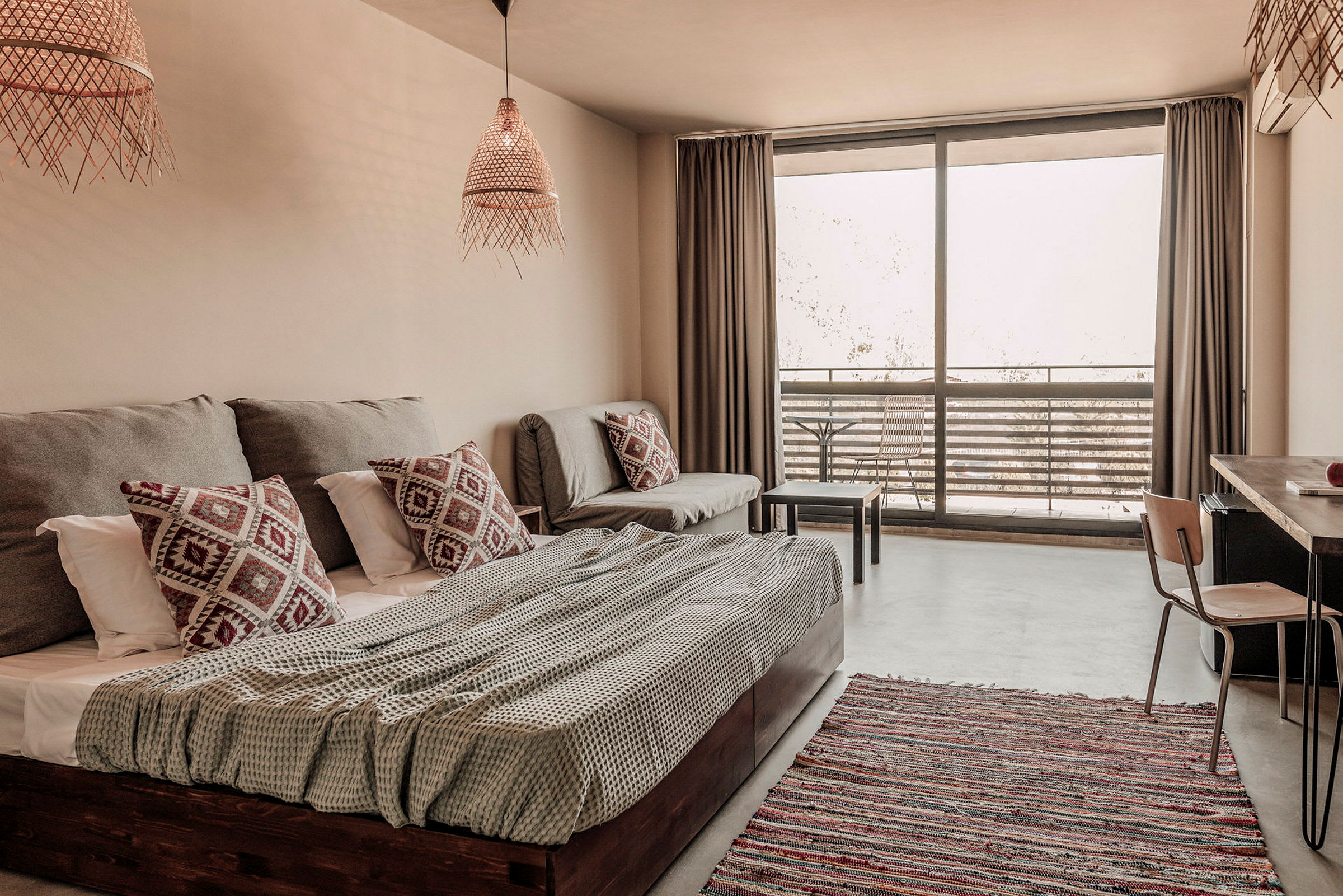 Et lyst og moderne hotelværelse med seng, sofa og en altan med havemøbler. (AI-genereret tekst)