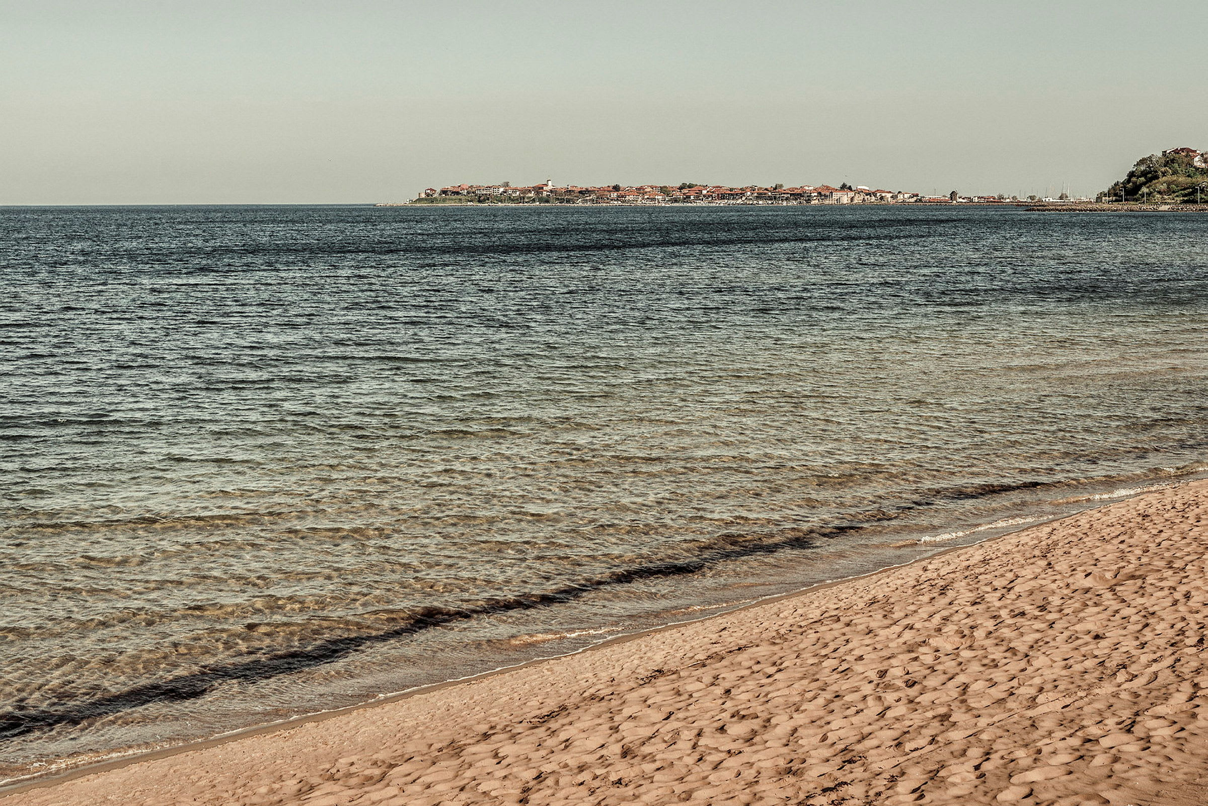 Billede af en sandstrand ved havet med en by i baggrunden. (AI-genereret tekst)