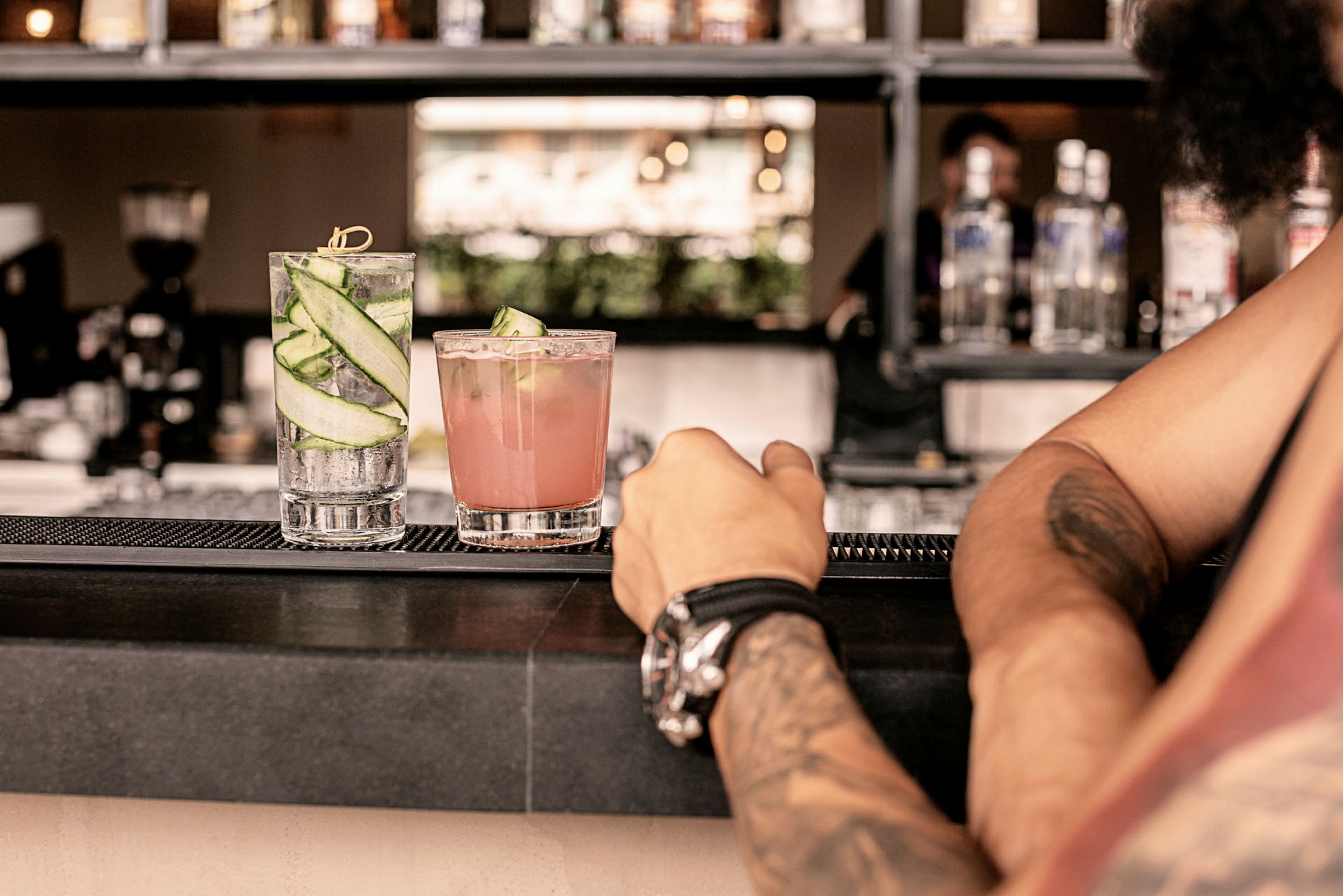 To cocktails på en bardisk, med en persons arm i forgrunden. (AI-genereret tekst)