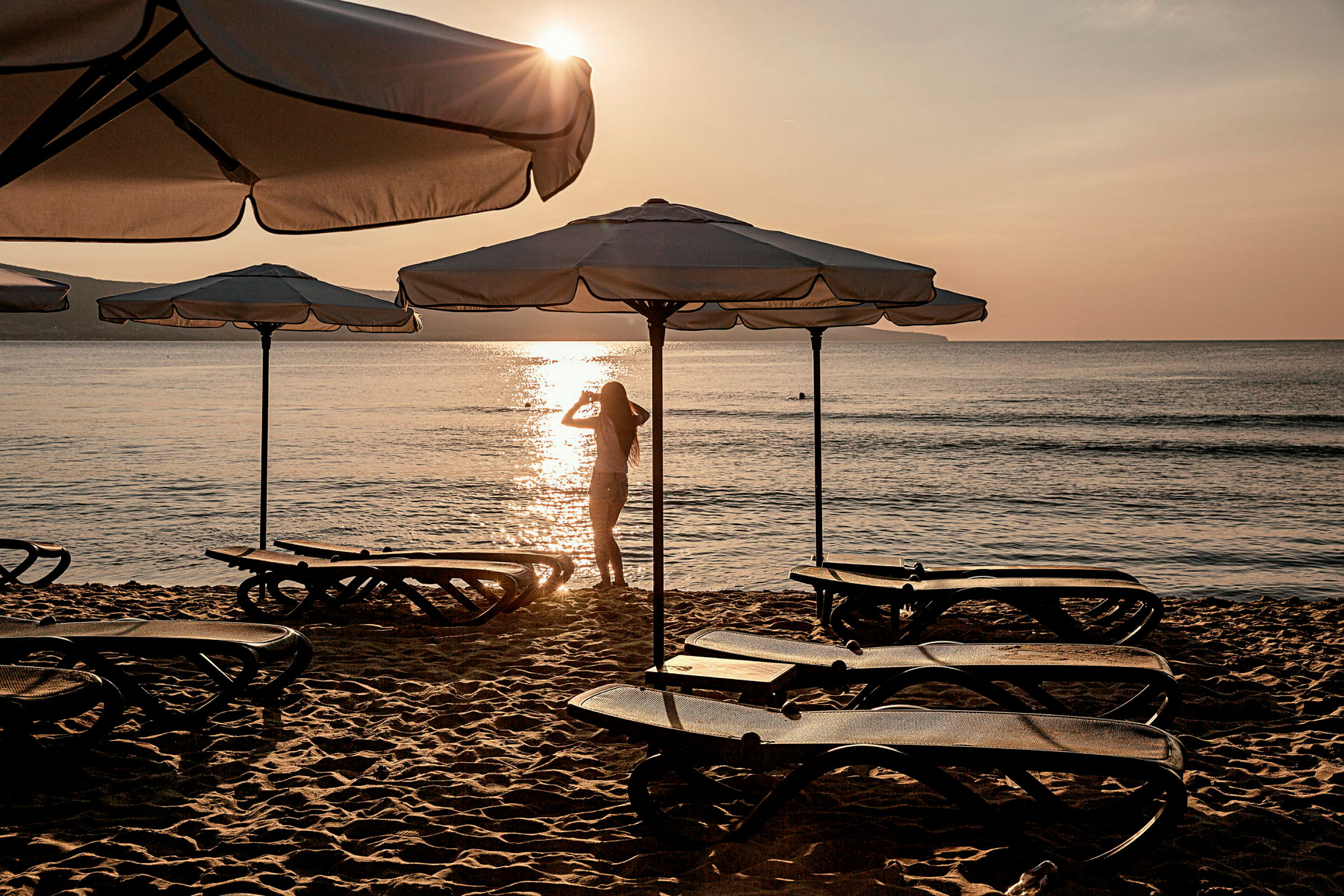 Solsenge og parasoller på en sandstrand ved solnedgang. (AI-genereret tekst)