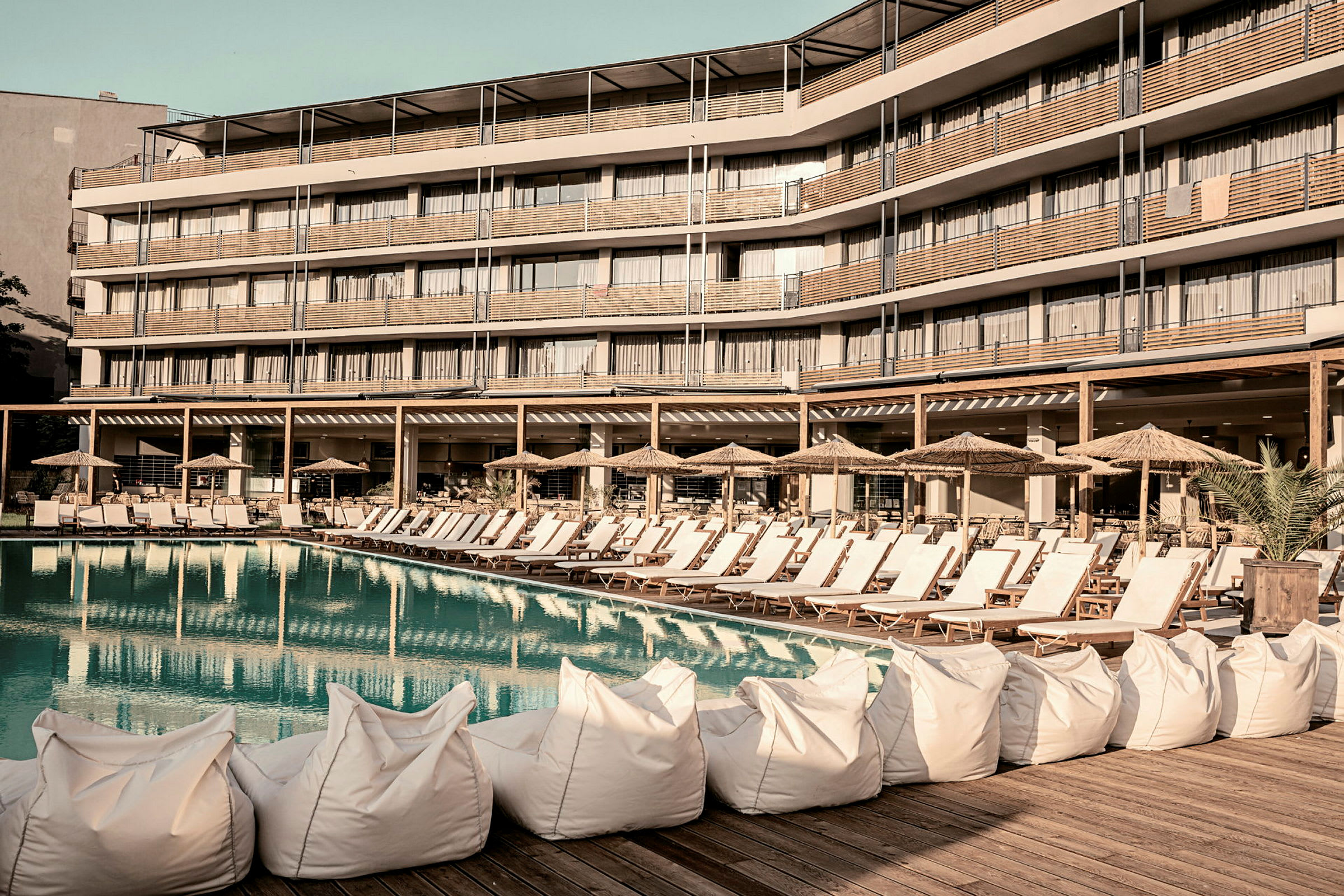 Liggestole og parasoller ved en pool foran et hotel. (AI-genereret tekst)
