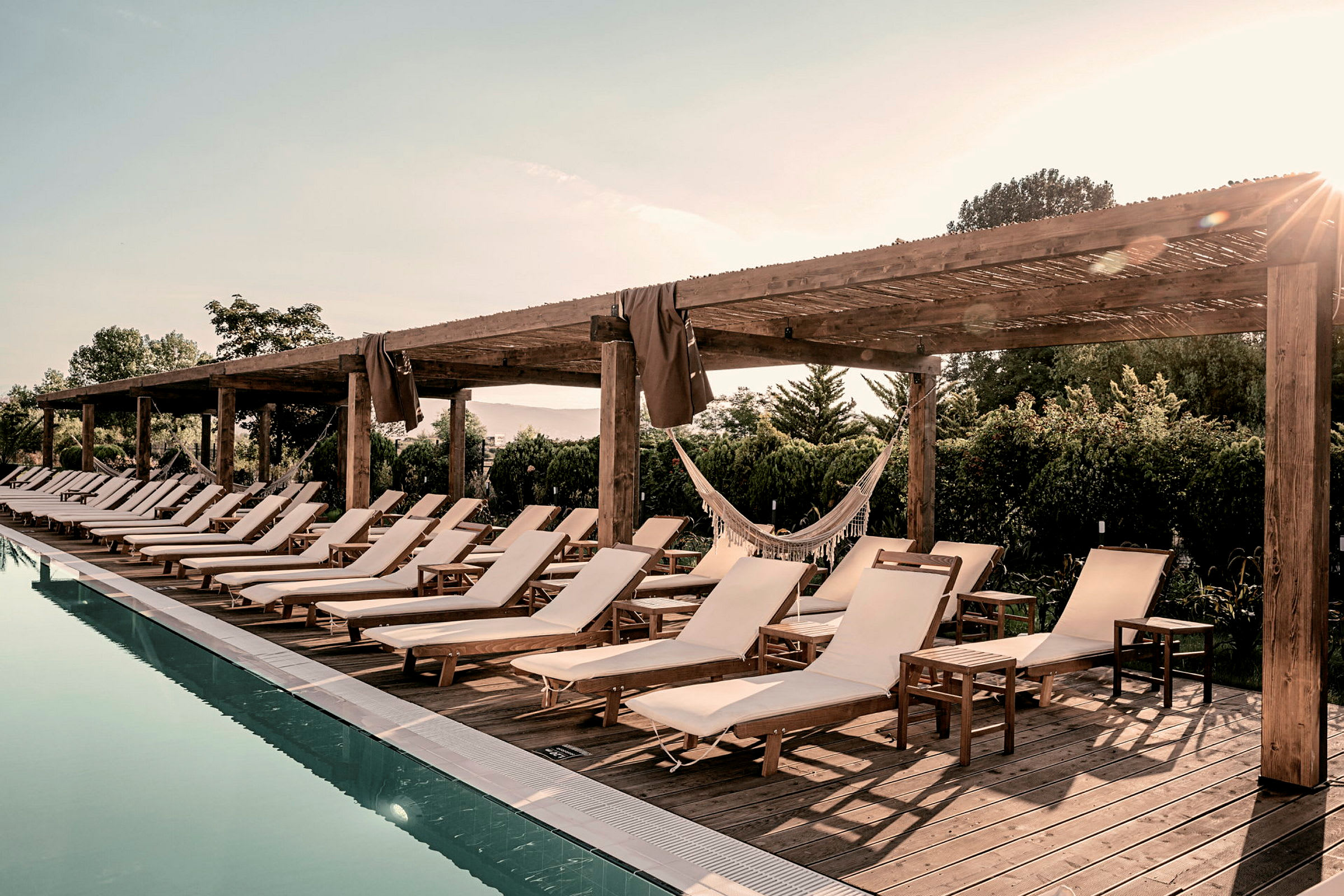 Liggestole ved en pool under en træpergola. (AI-genereret tekst)