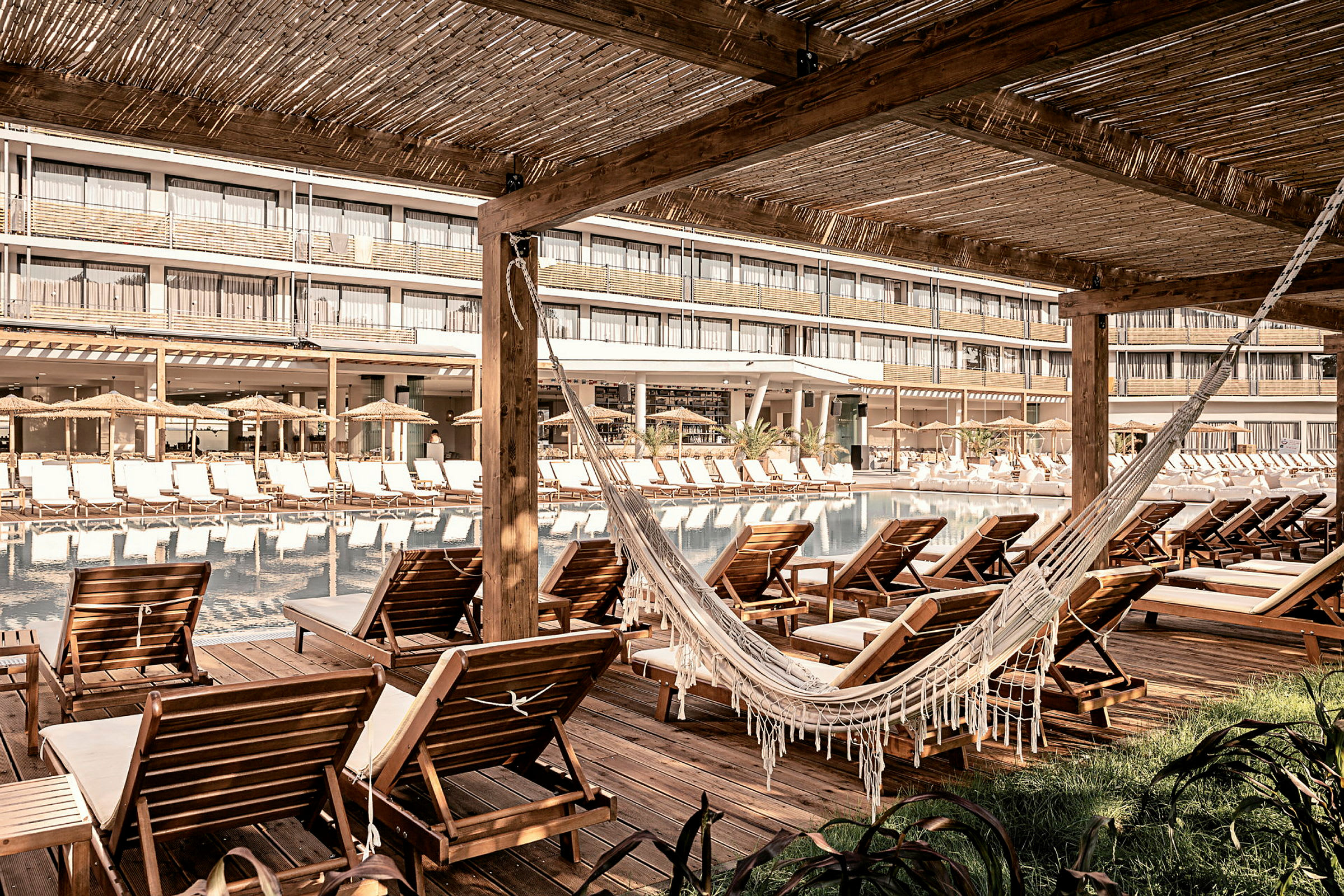 Stole og en hængekøje ved en pool, med hotelbygningen i baggrunden. (AI-genereret tekst)