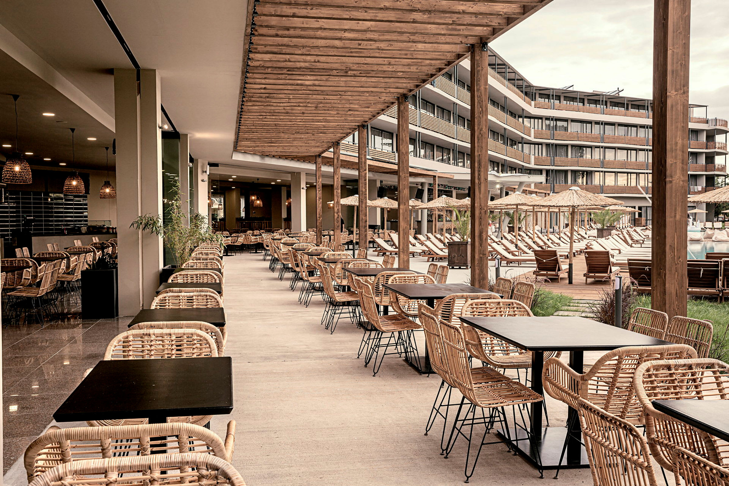 En udendørs restaurant med rottingmøbler og udsigt over en pool og solsenge. (AI-genereret tekst)