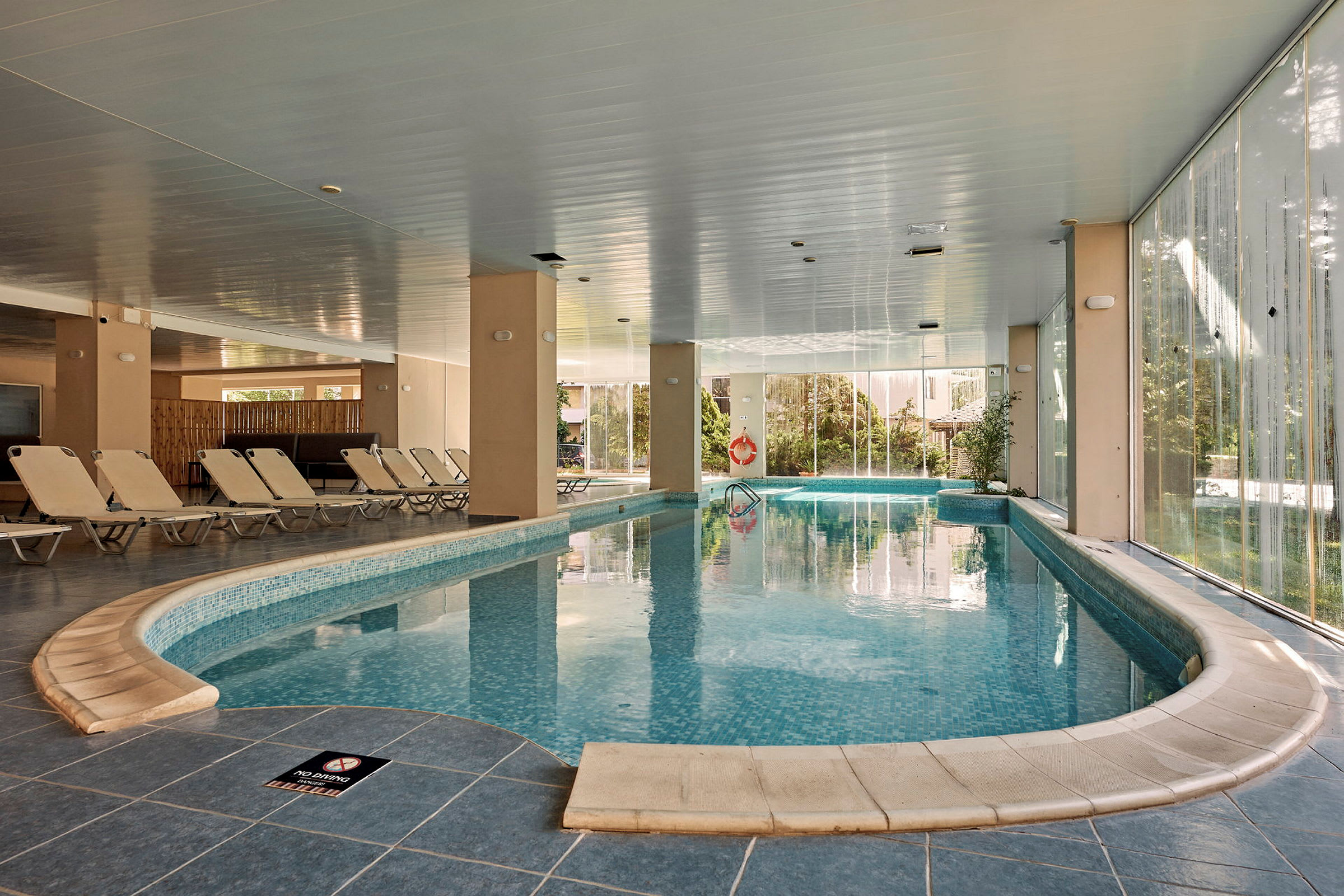 Indendørs swimmingpool med liggestole langs siden og glasvægge. (AI-genereret tekst)