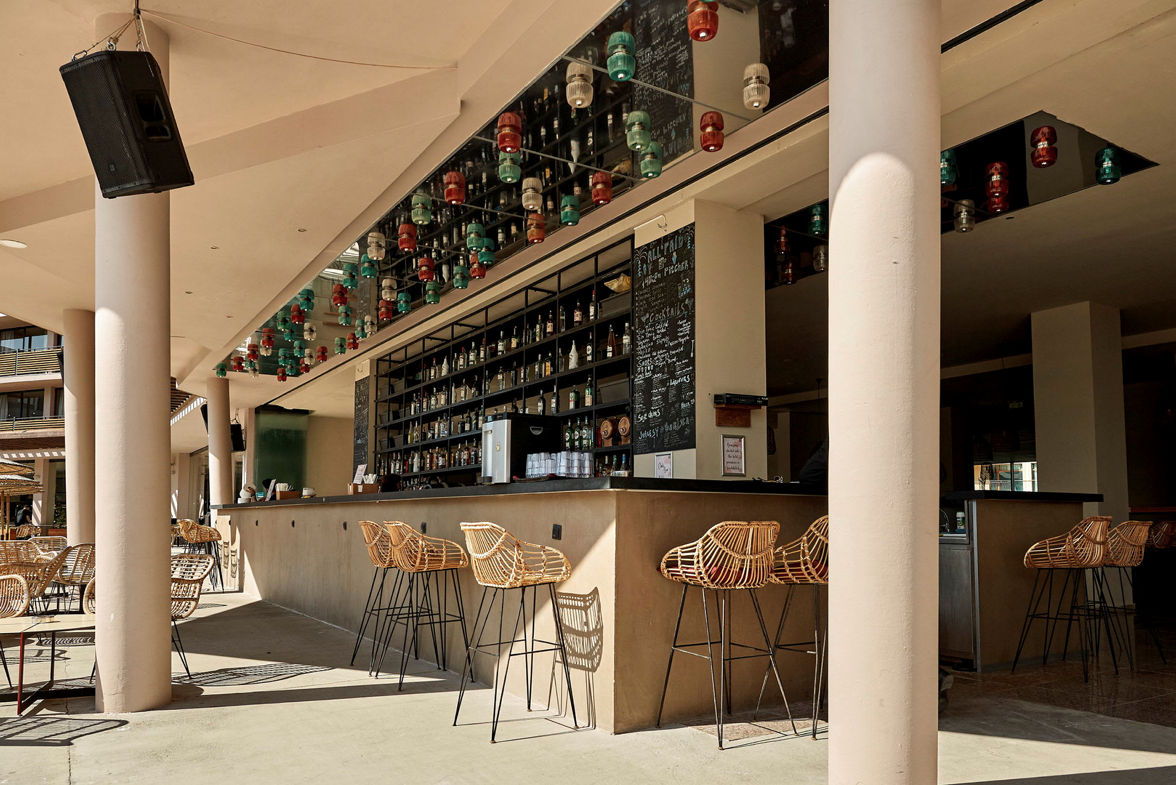 En udendørs bar med rottinstole og et spejlet loft dekoreret med lamper. (AI-genereret tekst)