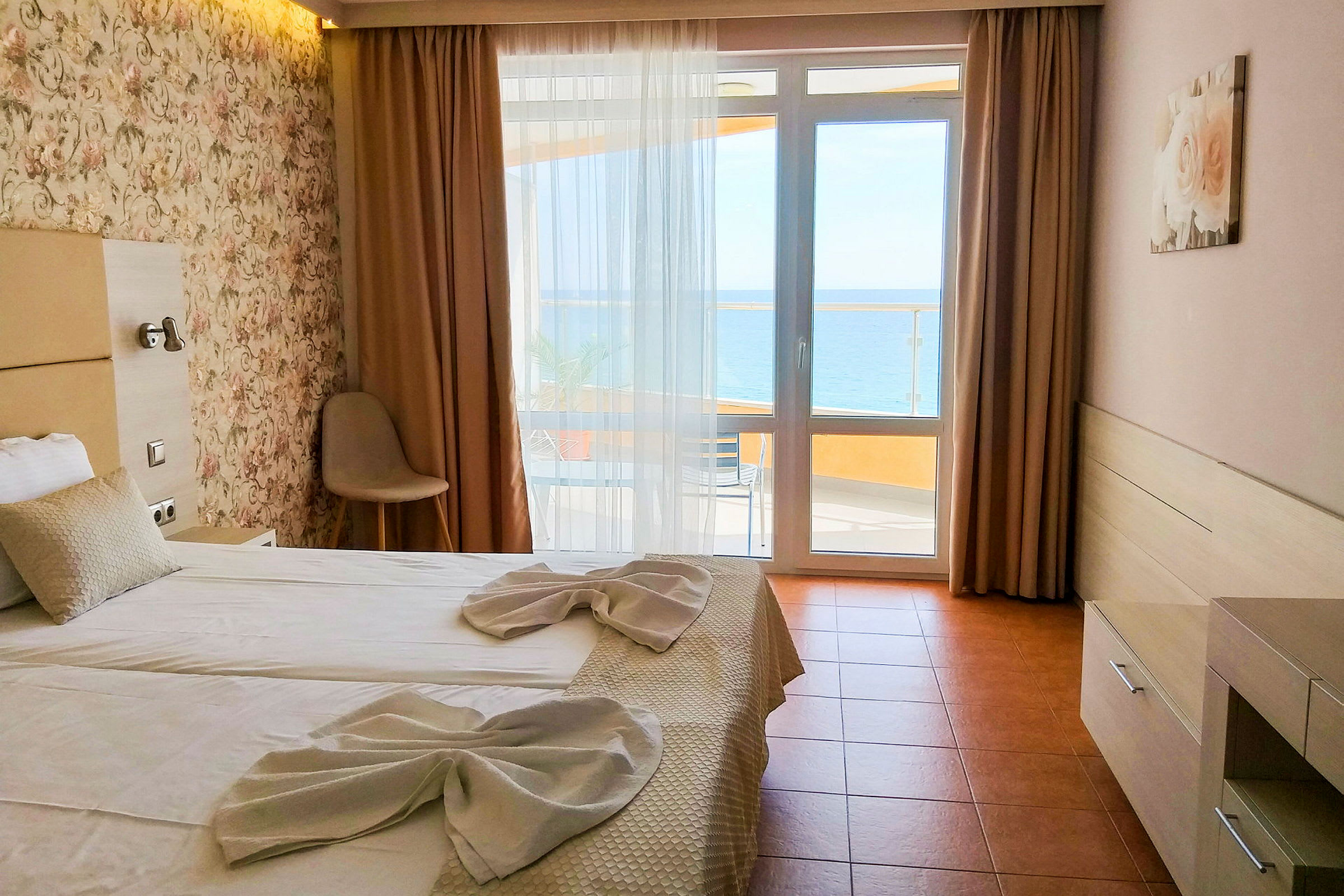 Et hotelværelse med en dobbeltseng opredt med hvide lagner og dekoreret med håndklæder. Der er et vindue med udsigt til havet. (AI-genereret tekst)
