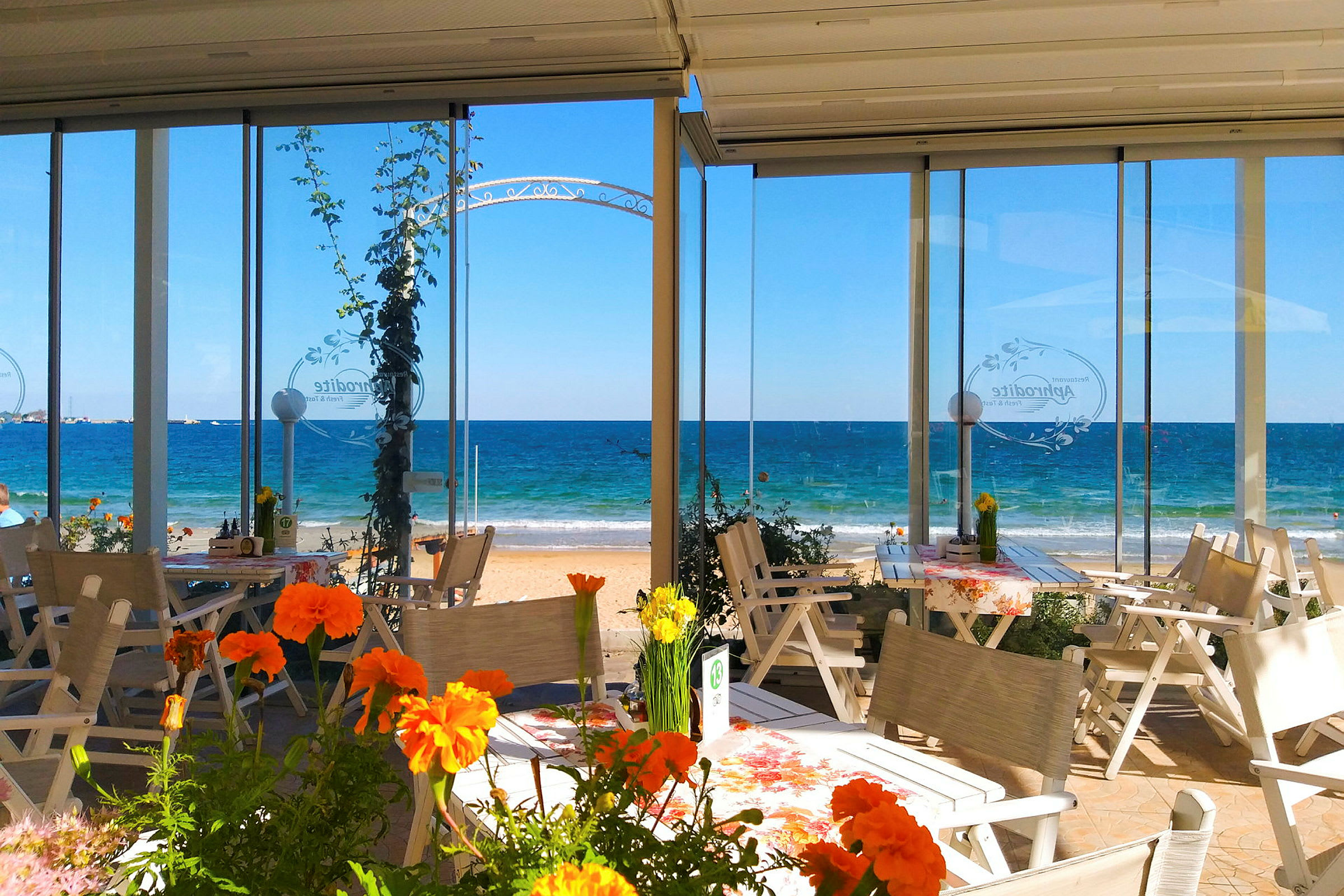 Udendørs serveringsområde med blomster og udsigt til havet. (AI-genereret tekst)
