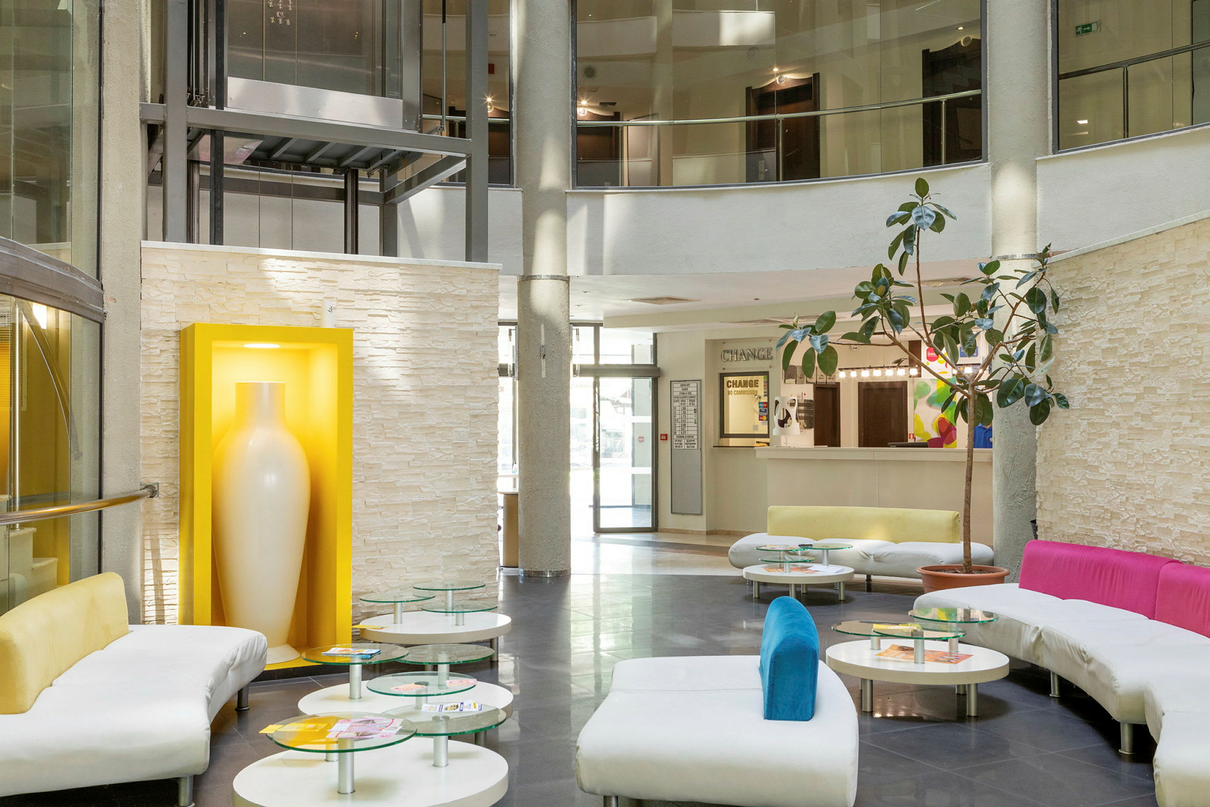 En moderne hotellobby med sofaer, glasborde og en stor hvid vase i en gul ramme. (AI-genereret tekst)