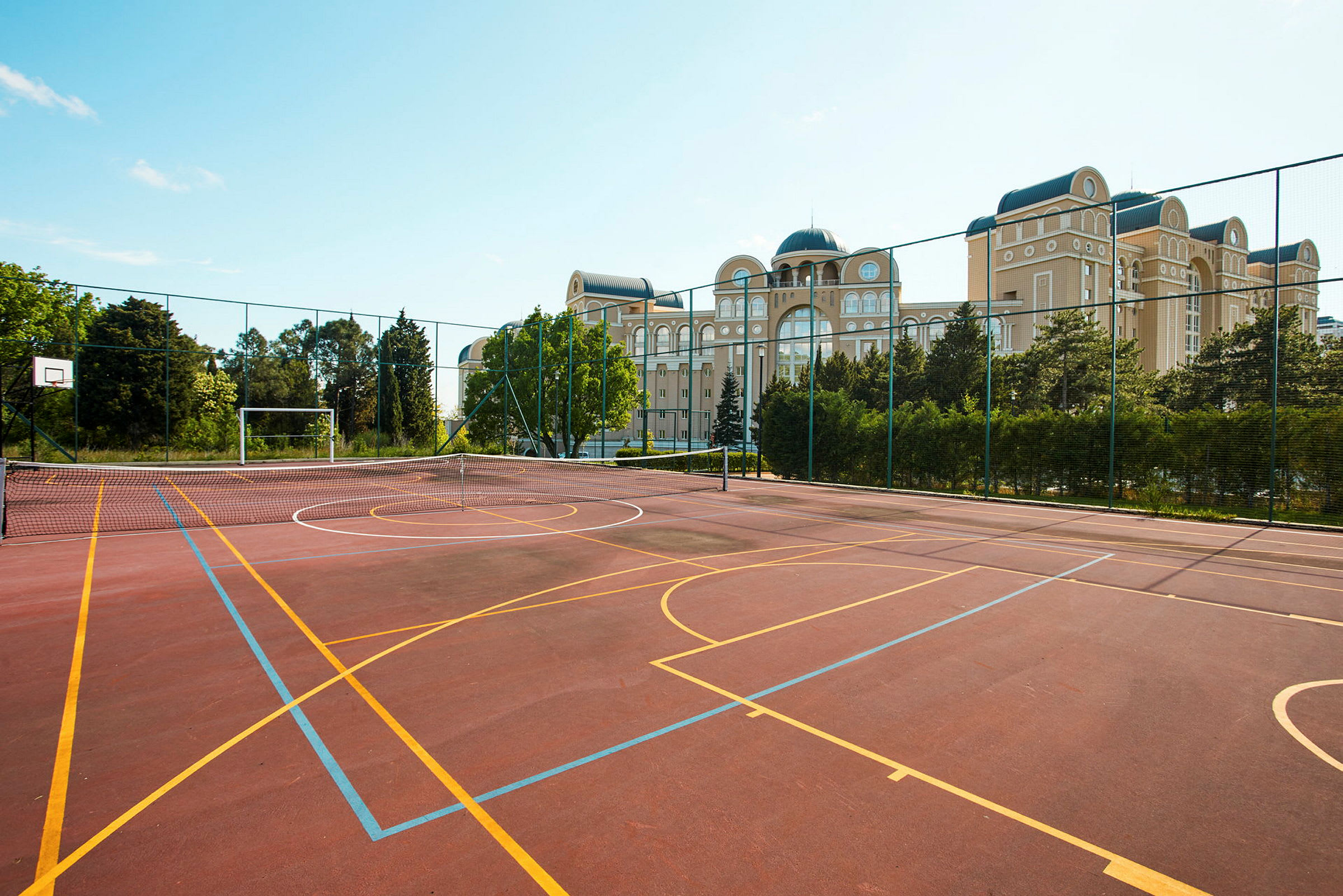 En sportsbane med en basketballkurv og målbur. I baggrunden ses bygninger og grønne områder. (AI-genereret tekst)