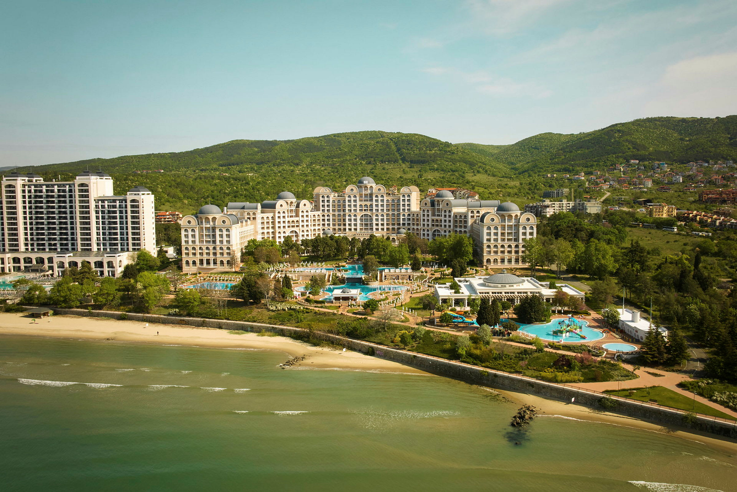 Udsigt over hotelkompleks ved stranden med pools og frodige omgivelser. (AI-genereret tekst)