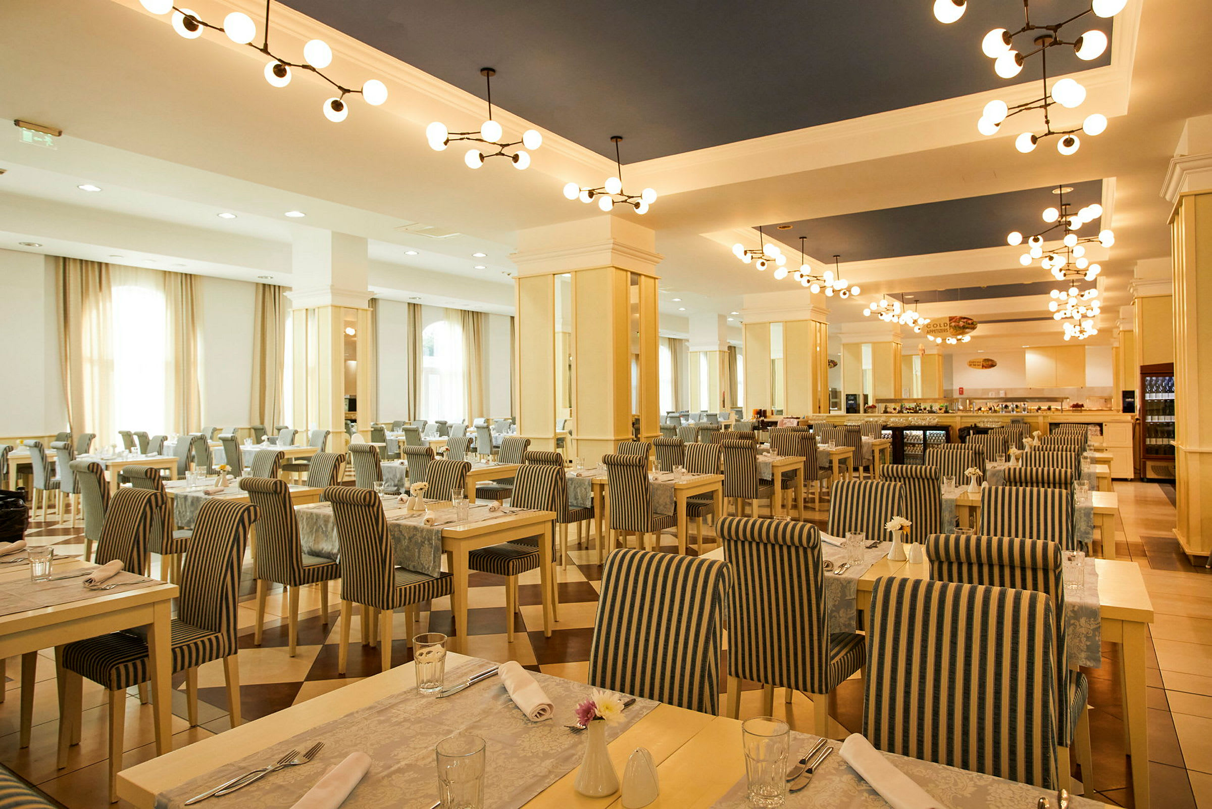 En rummelig restaurant med borde og stole i stribet stof og loftslamper i moderne design. (AI-genereret tekst)