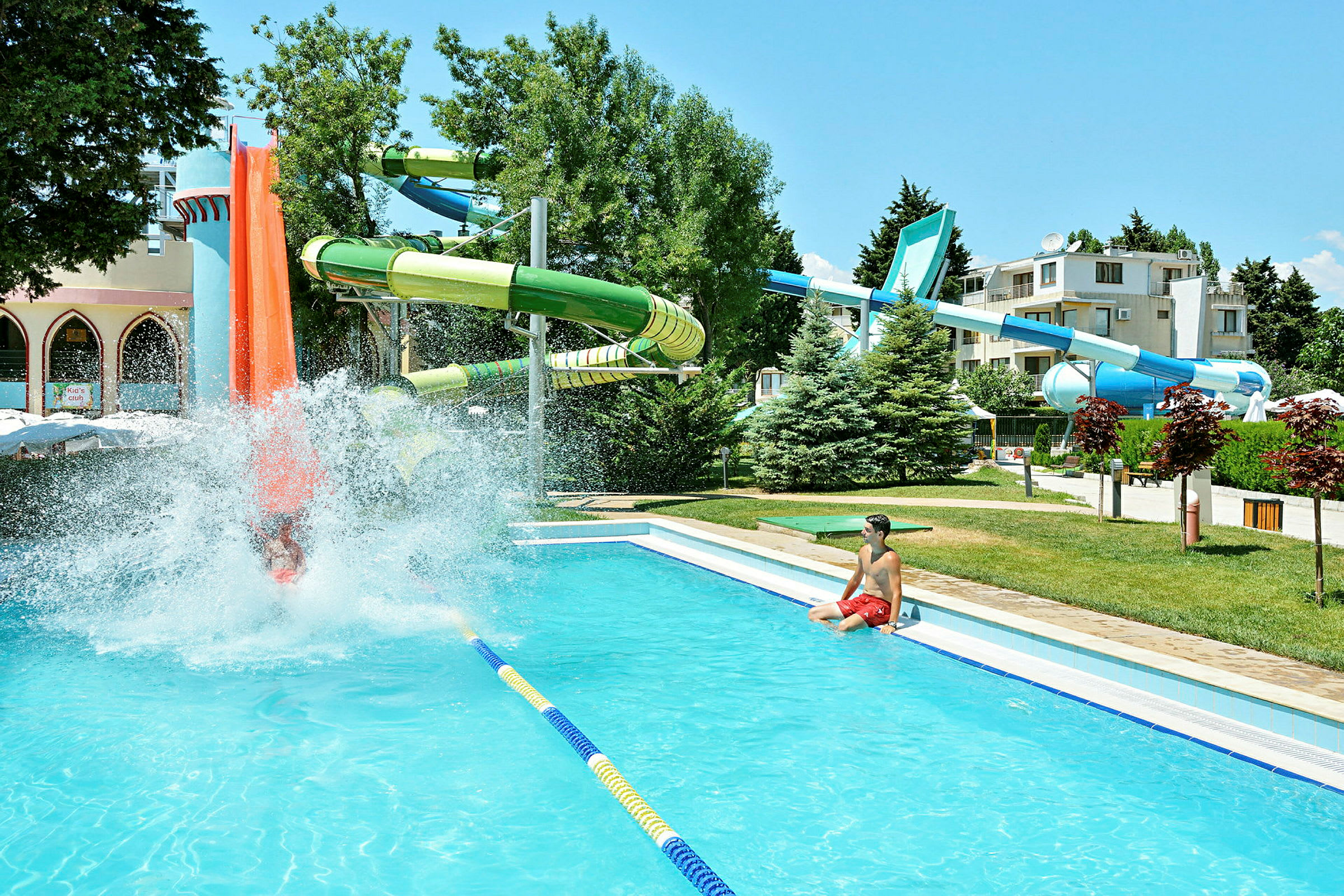 En vandpark med rutsjebaner og en pool, omgivet af beplantning og bygninger. (AI-genereret tekst)