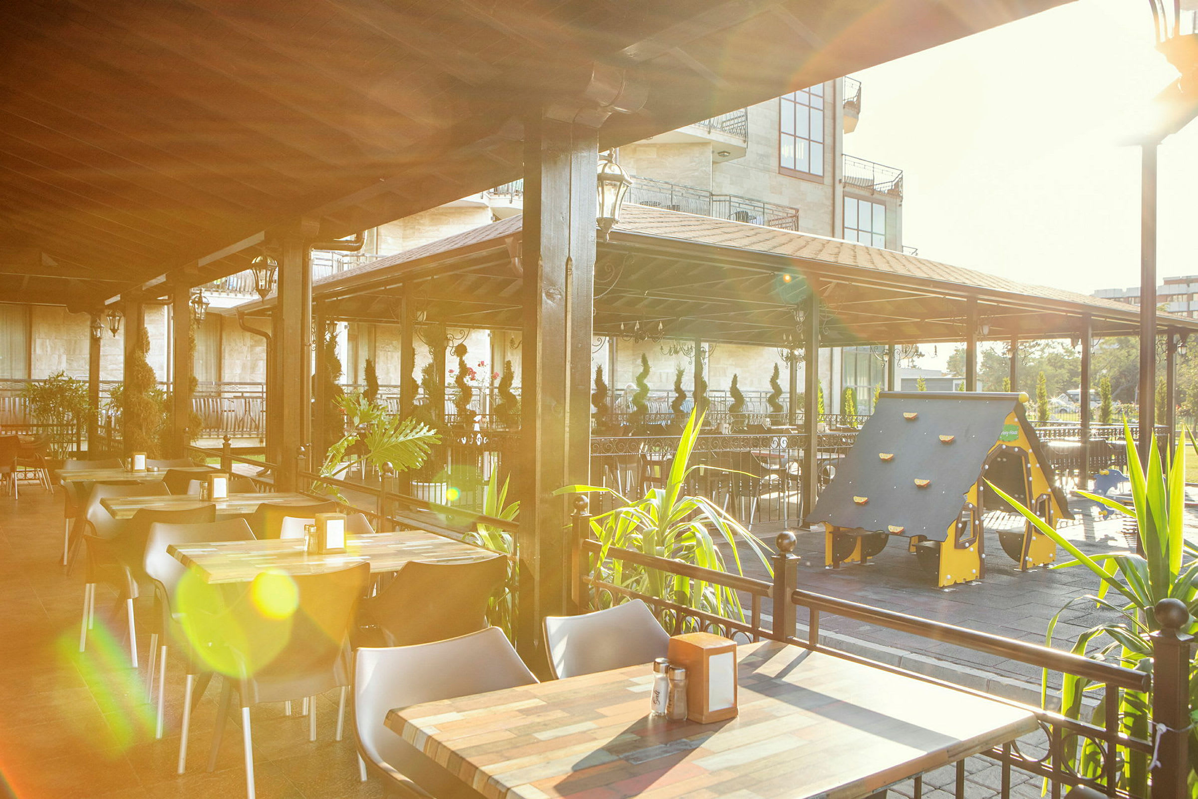 En udendørs restaurant med borde, stole og en legeplads til børn under et tag. (AI-genereret tekst)