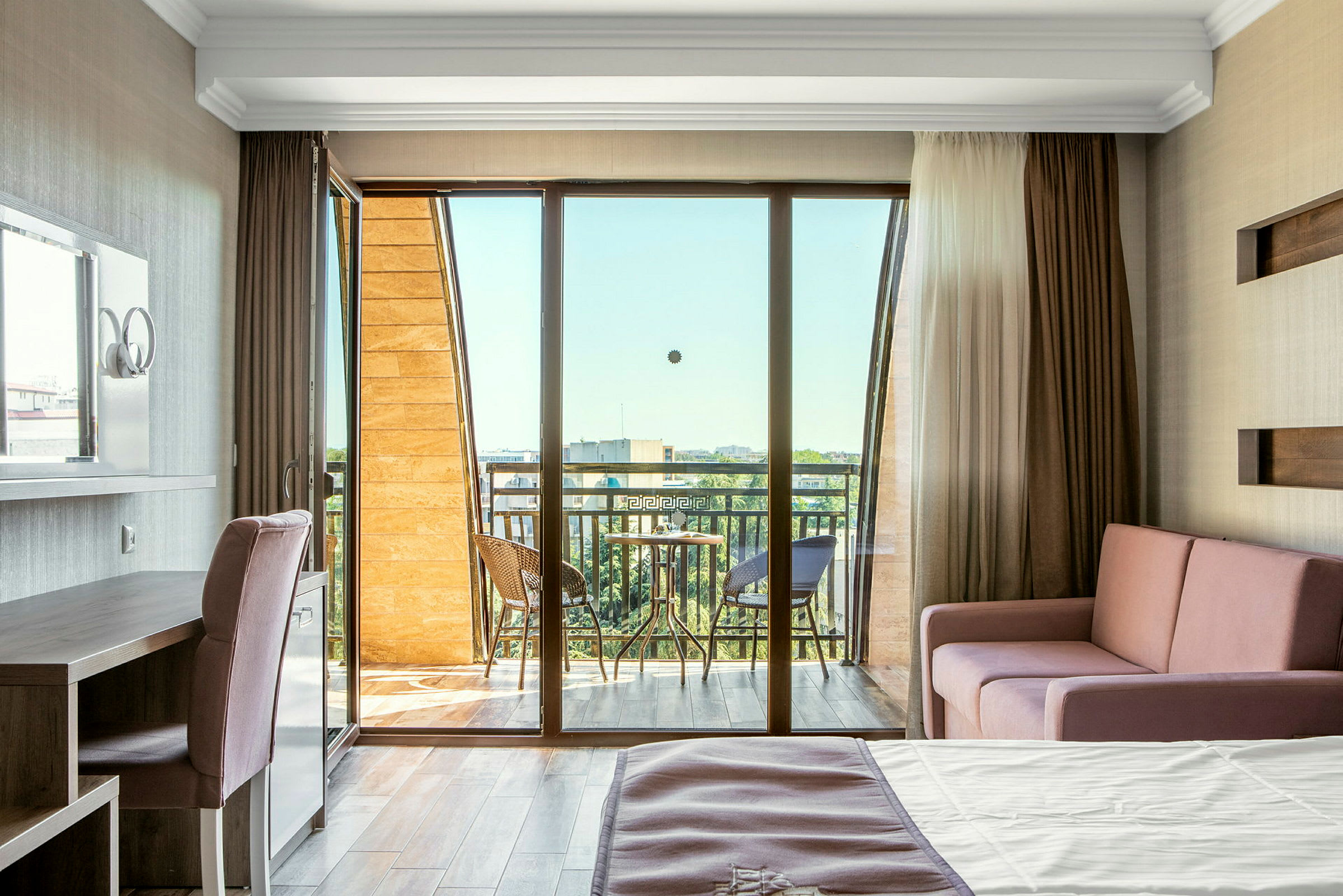 Et lyst hotelværelse med balkon, møbleret med seng, sofa og skrivebord. (AI-genereret tekst)