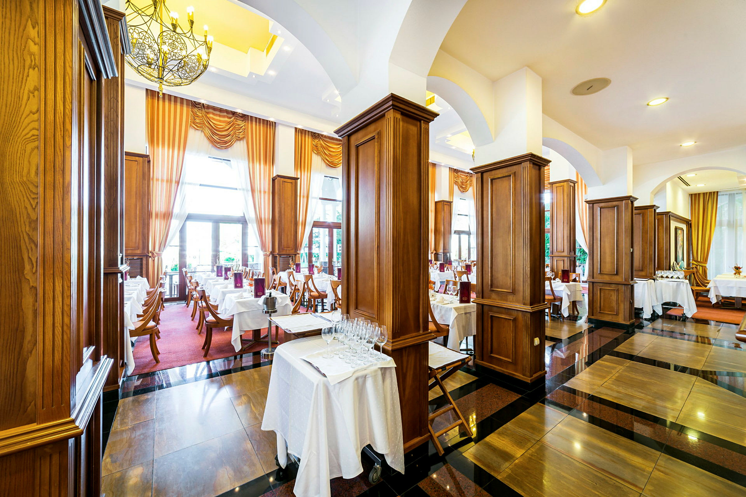 En elegant restaurant med dækkede borde, mørke trægulve og store vinduer med gardiner. (AI-genereret tekst)