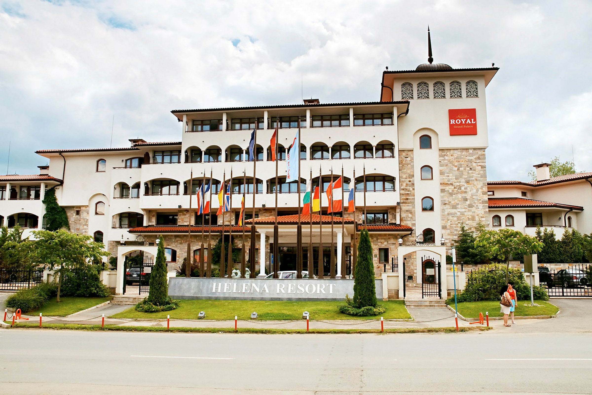 Et hotel i flere etager med moderne arkitektur, med flag foran og teksten 'Helena Resort' på et skilt. (AI-genereret tekst)