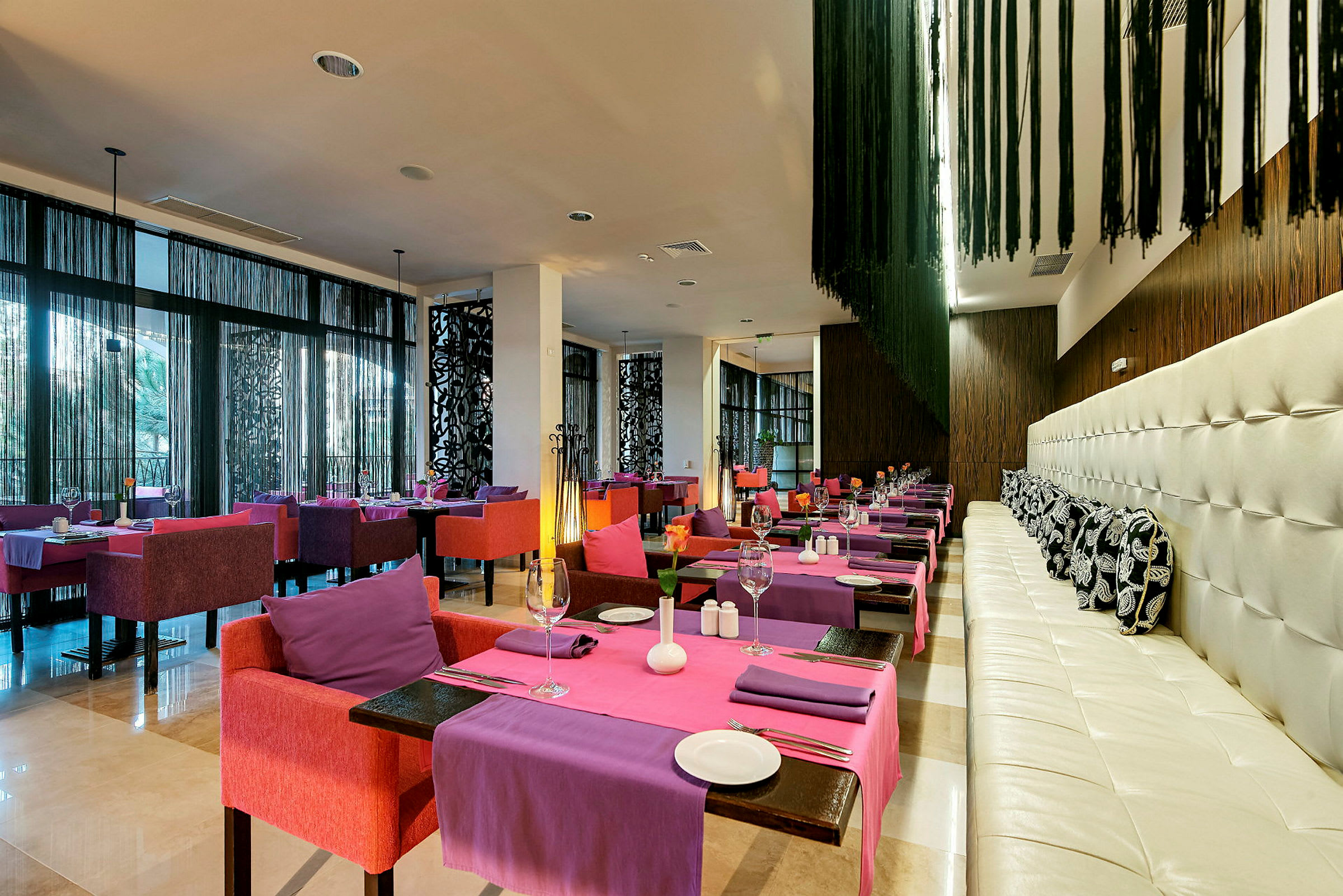 Et moderne indrettet restaurantområde med farverige stole og borde dækket med lilla og lyserøde duge. (AI-genereret tekst)