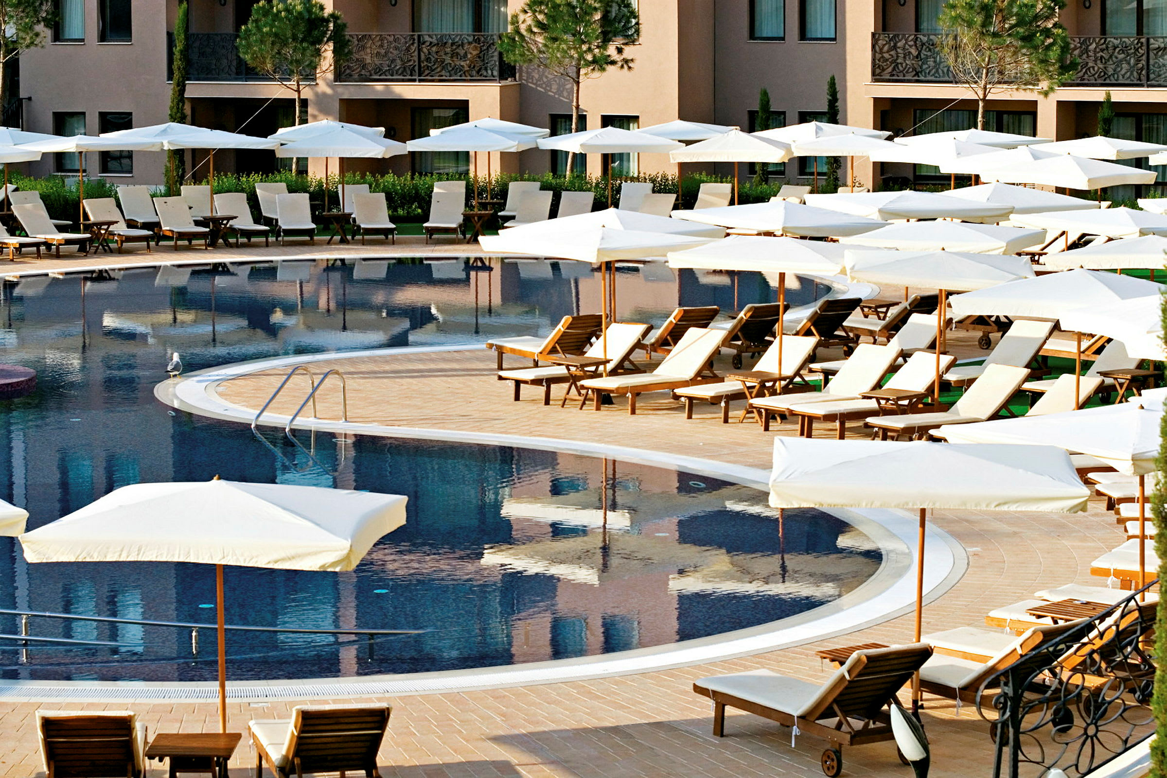 Billede af en pool omgivet af liggestole og parasoller ved et hotel. (AI-genereret tekst)