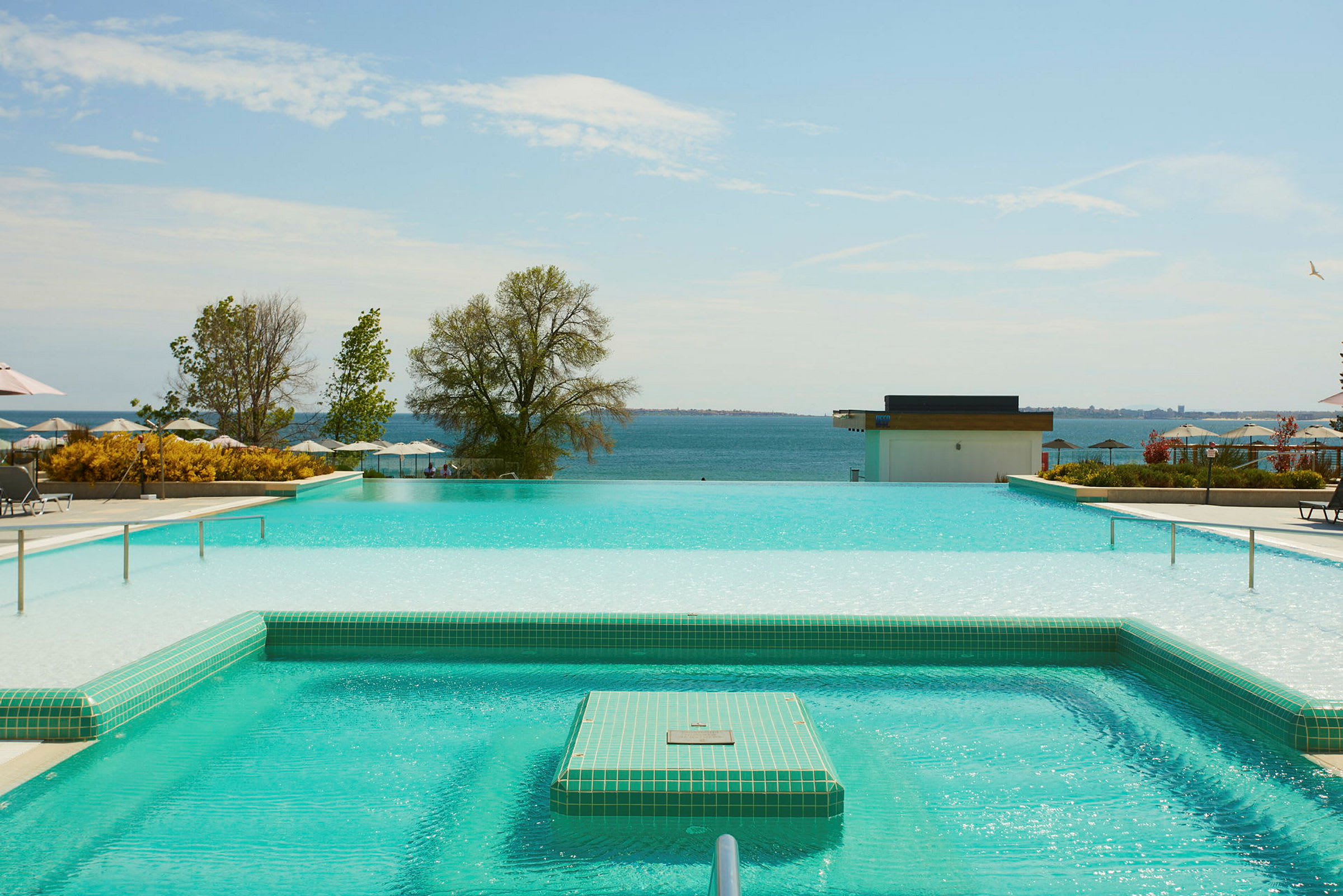 En infinitypool med udsigt over havet og den omkringliggende grønne natur. (AI-genereret tekst)