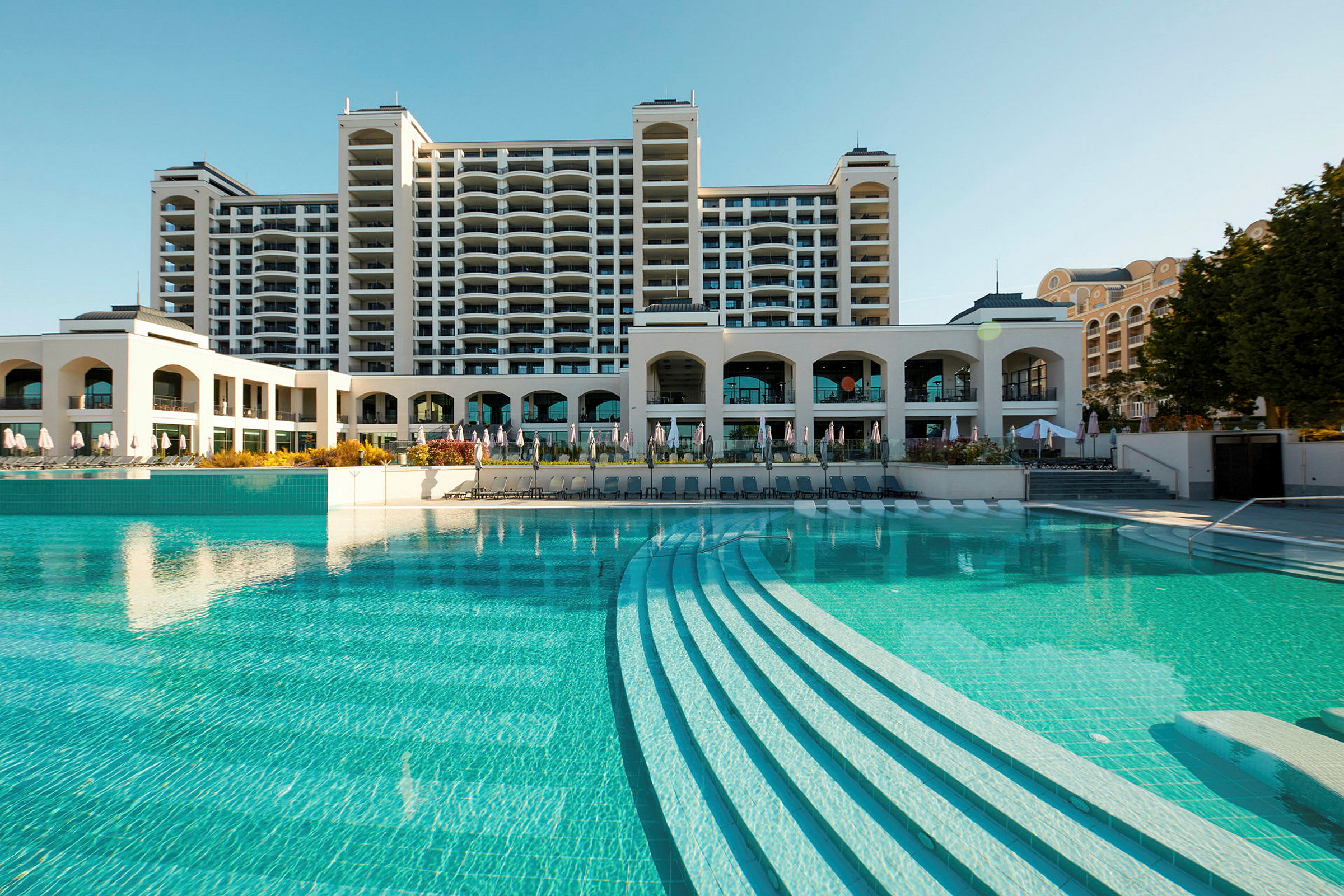 Hotelbygning ved en stor udendørs swimmingpool. (AI-genereret tekst)