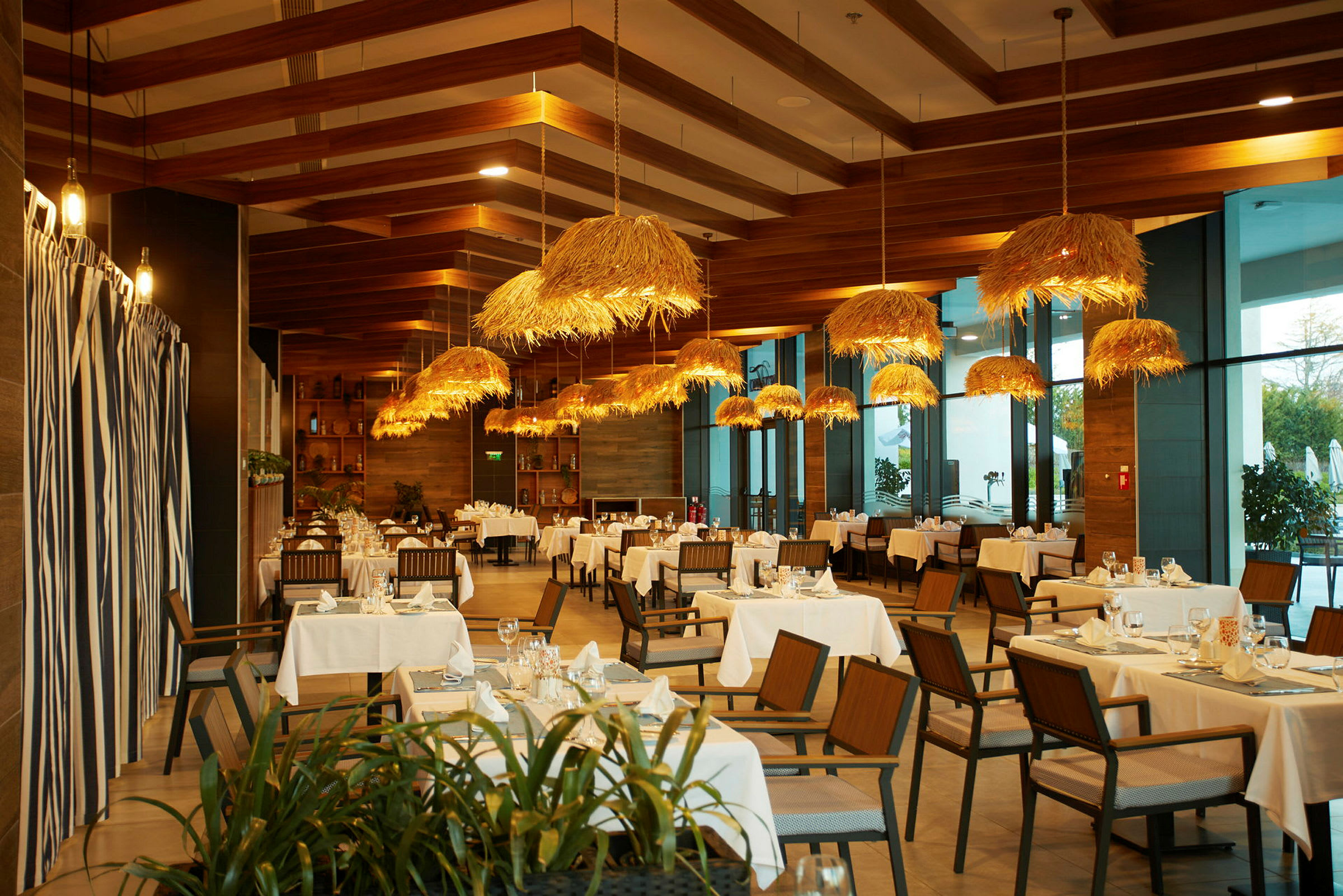 Restaurant med borde, træstole og hængende lamper med halmdetaljer. (AI-genereret tekst)