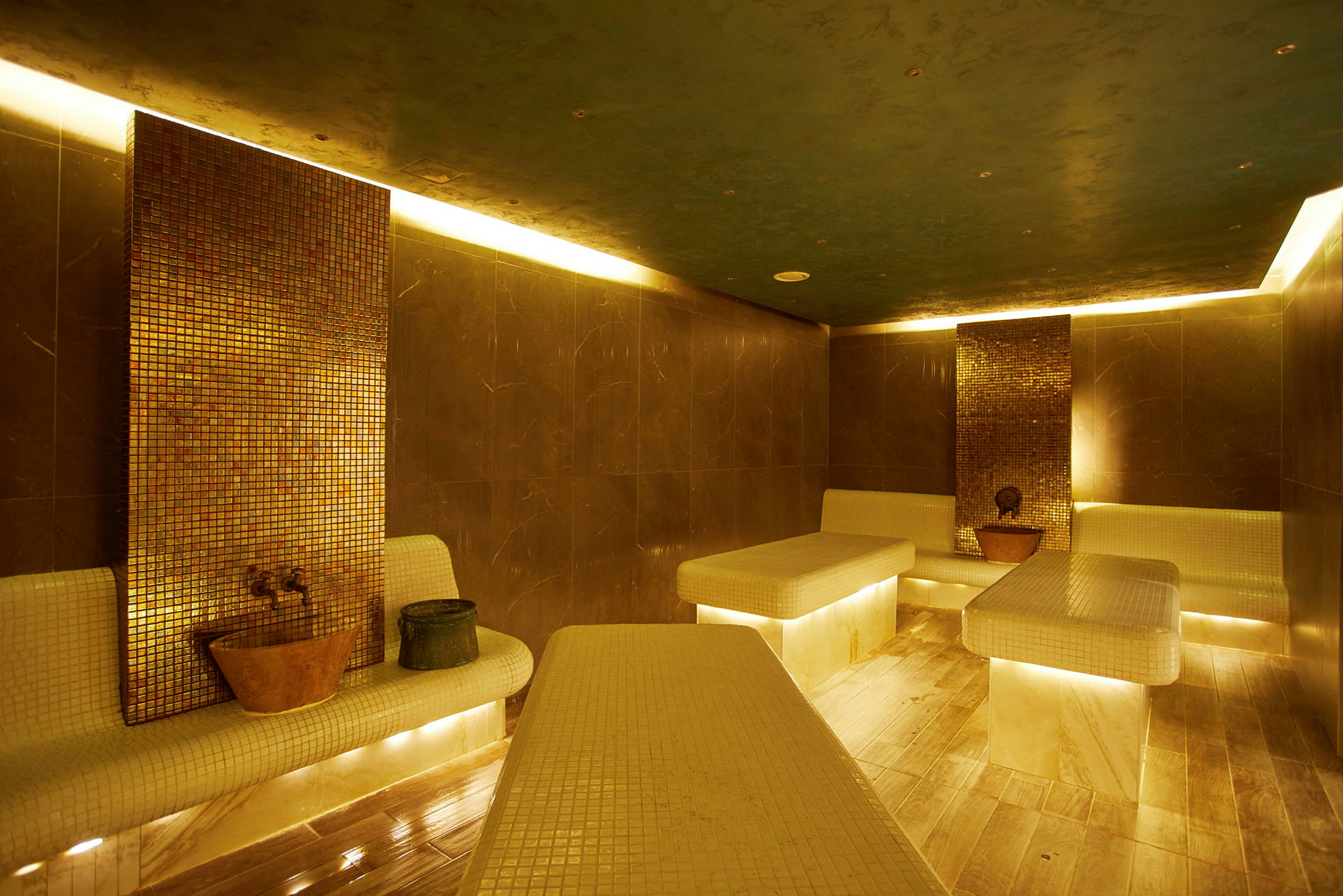 Indendørsbillede af et tyrkisk hamam med mosaikvægge og belyste marmorbænke. (AI-genereret tekst)