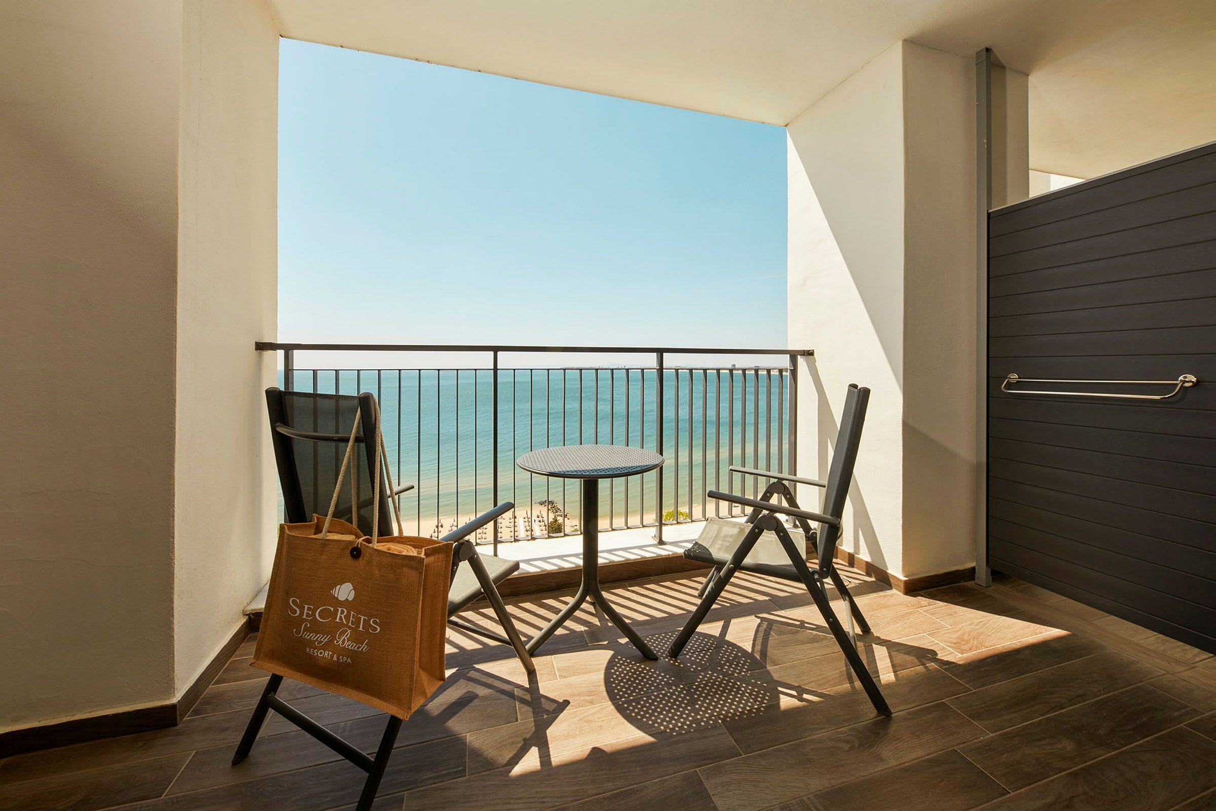 En balkon med to stole og et bord, udsigt til havet. (AI-genereret tekst)