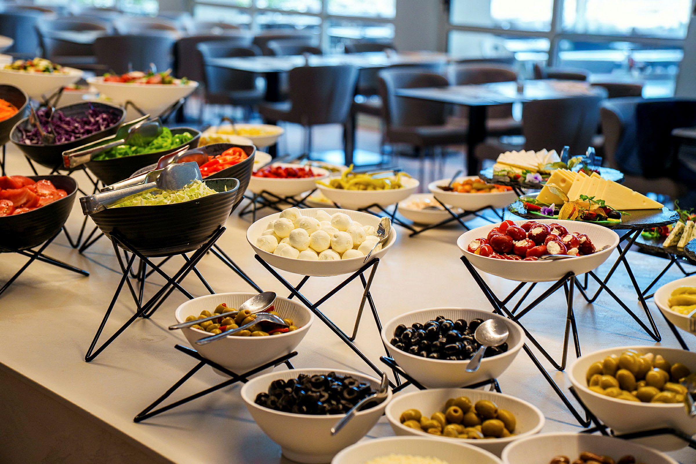 En buffet med forskellige skåle fyldt med grøntsager, oste og oliven i en restaurant. (AI-genereret tekst)