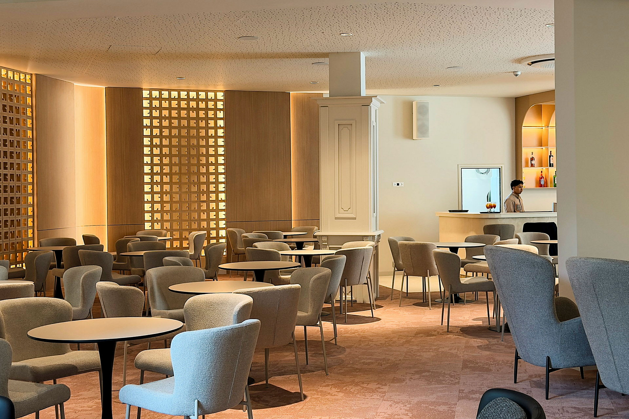 En moderne lounge med komfortable stole og borde. En person står ved en minimalistisk bardisk. (AI-genereret tekst)