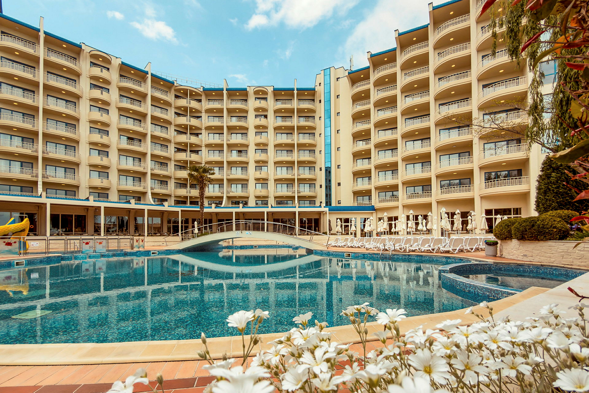 Et hotel med flere etager, der omkranser en udendørs pool og frodig have. (AI-genereret tekst)