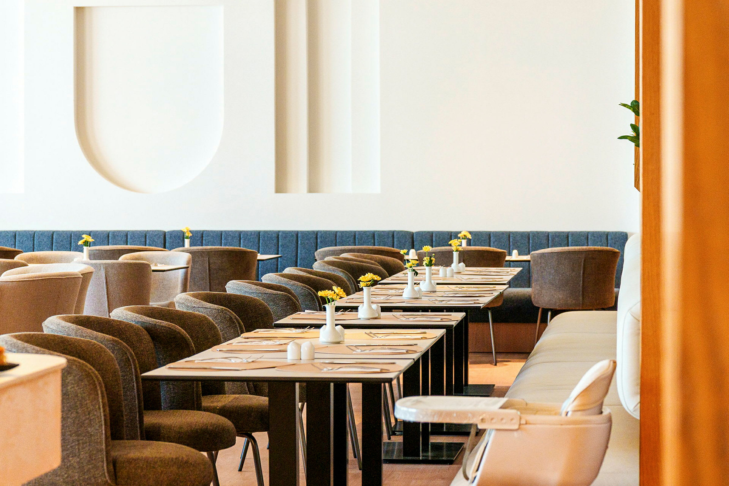 En elegant restaurant med moderne møbler, dækkede borde og små vaser med gule blomster. (AI-genereret tekst)