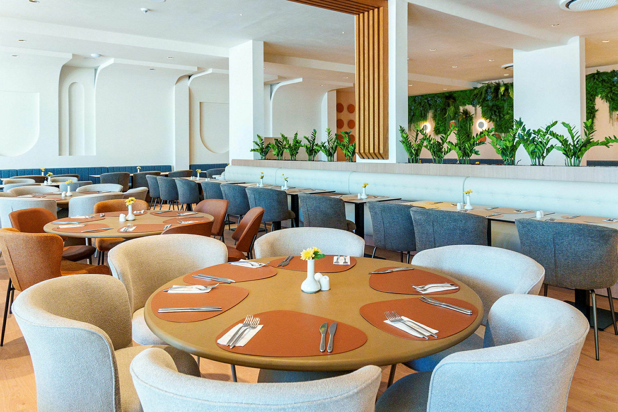 En restaurantinteriør med runde og rektangulære borde, elegante stole og grønne planter som dekoration. (AI-genereret tekst)