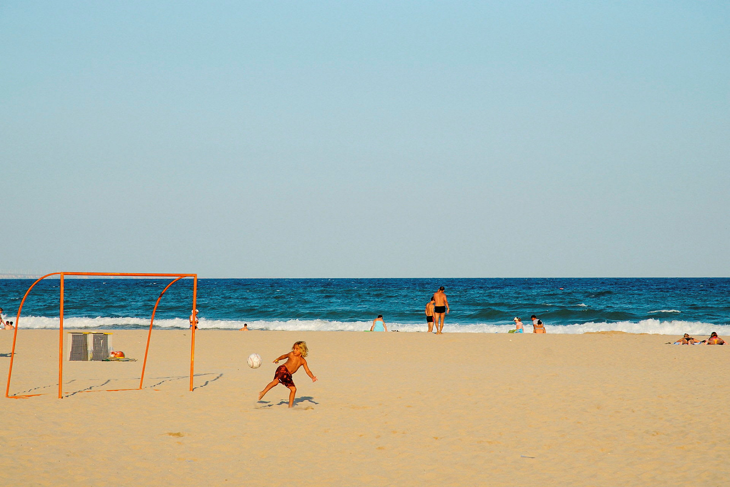 En strand med mennesker, der svømmer, og et sandfodboldmål. (AI-genereret tekst)