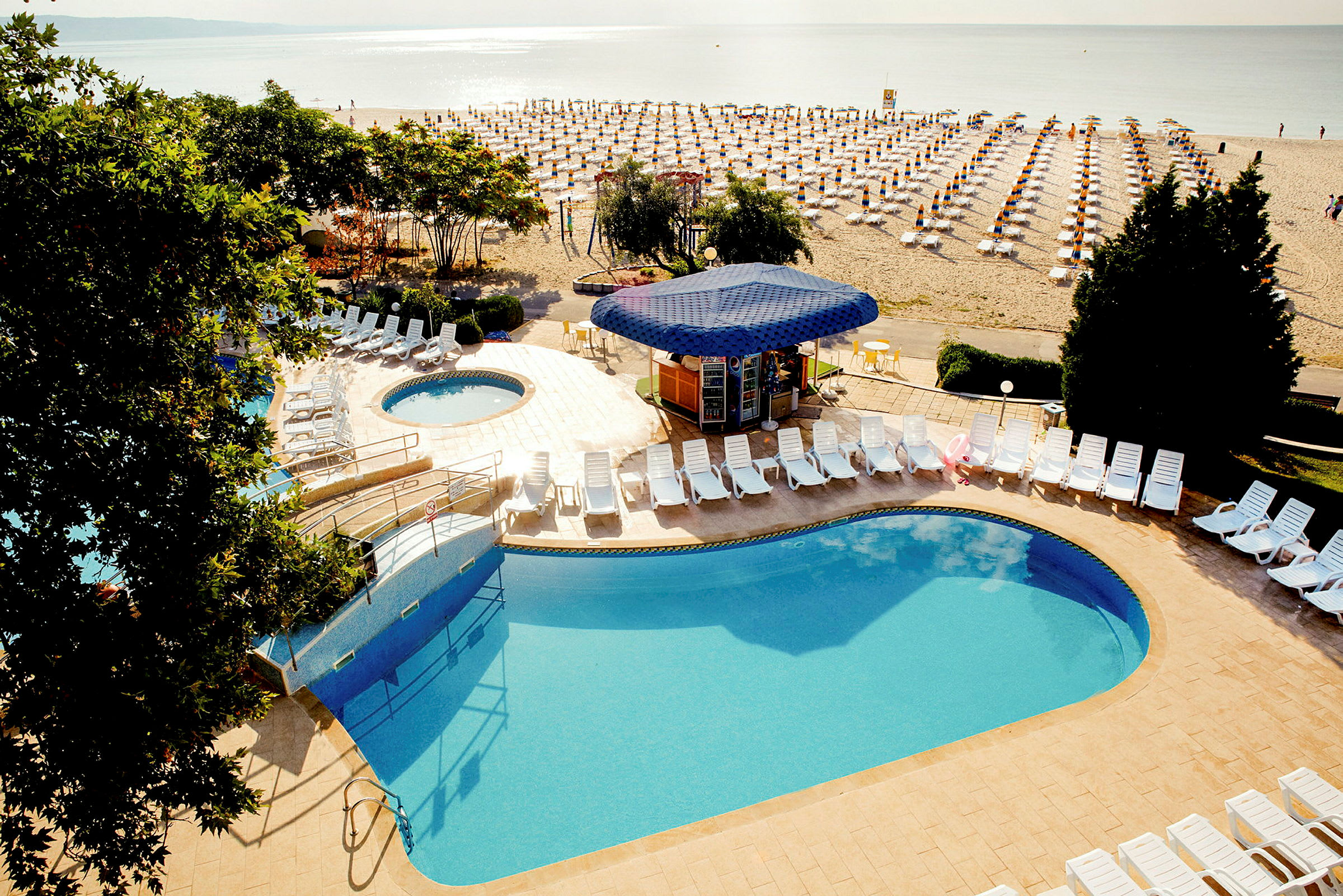Poolområde med liggestole og en strand med solvogne i baggrunden. (AI-genereret tekst)