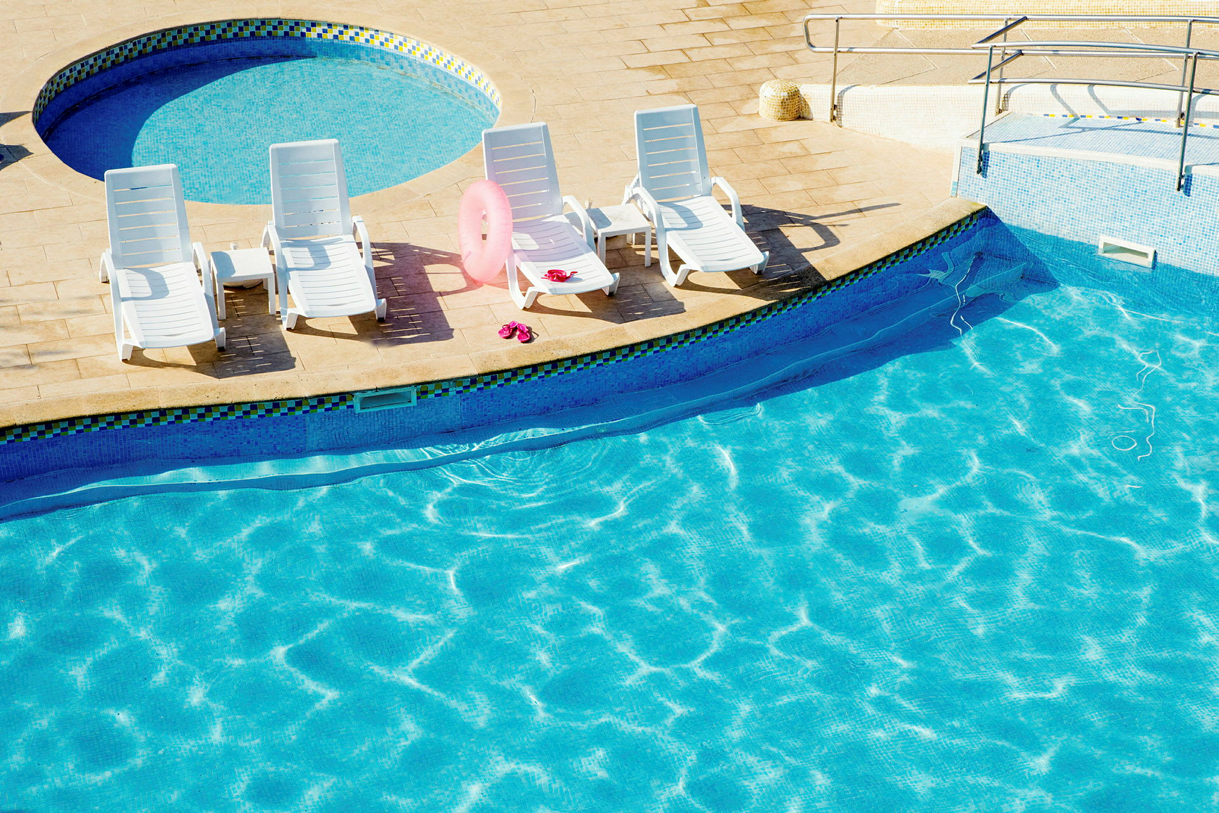 Fire liggestole på en terrasse ved en pool med klart vand. (AI-genereret tekst)