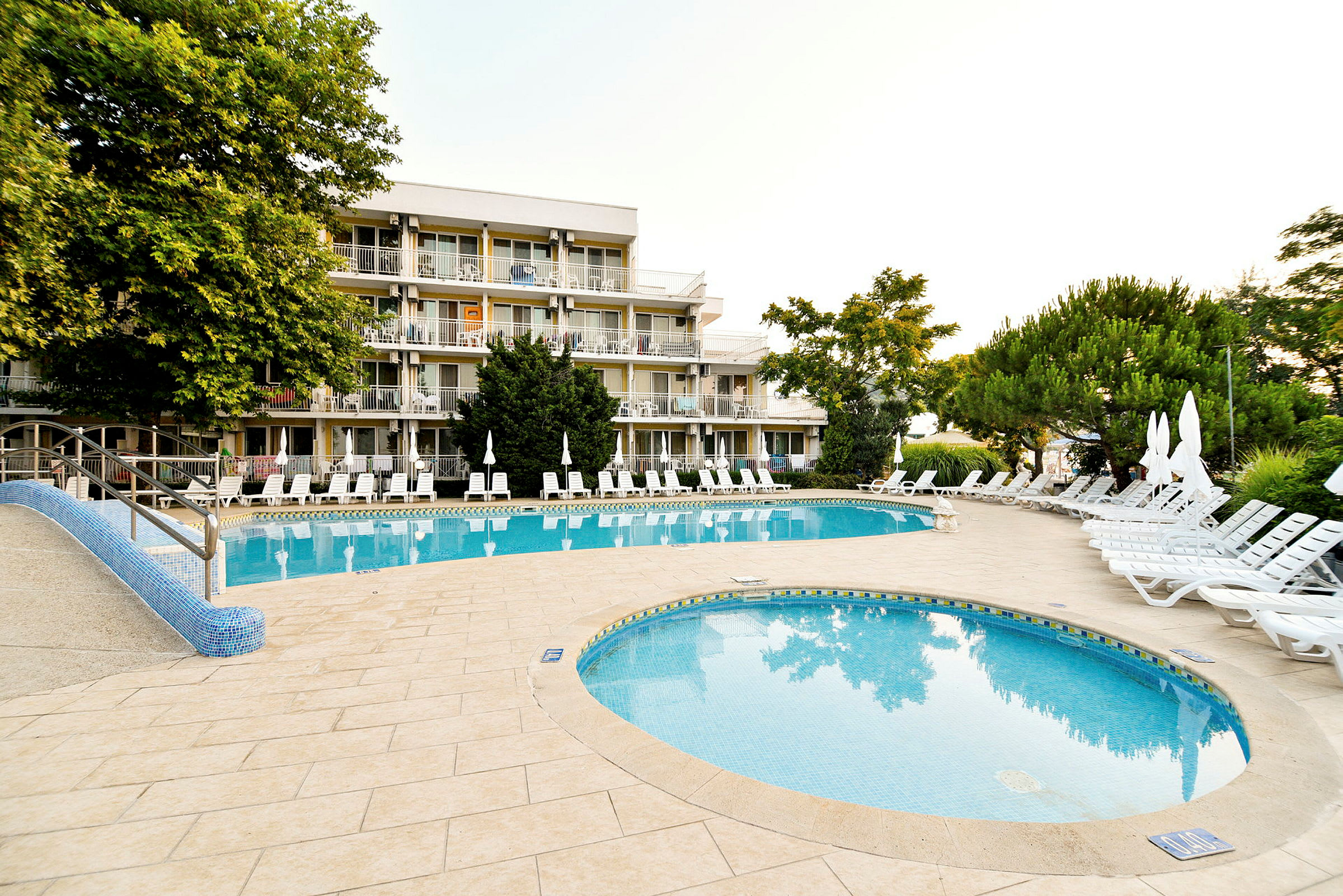 Hotellets poolområde med liggestole og omgivende grønt. (AI-genereret tekst)