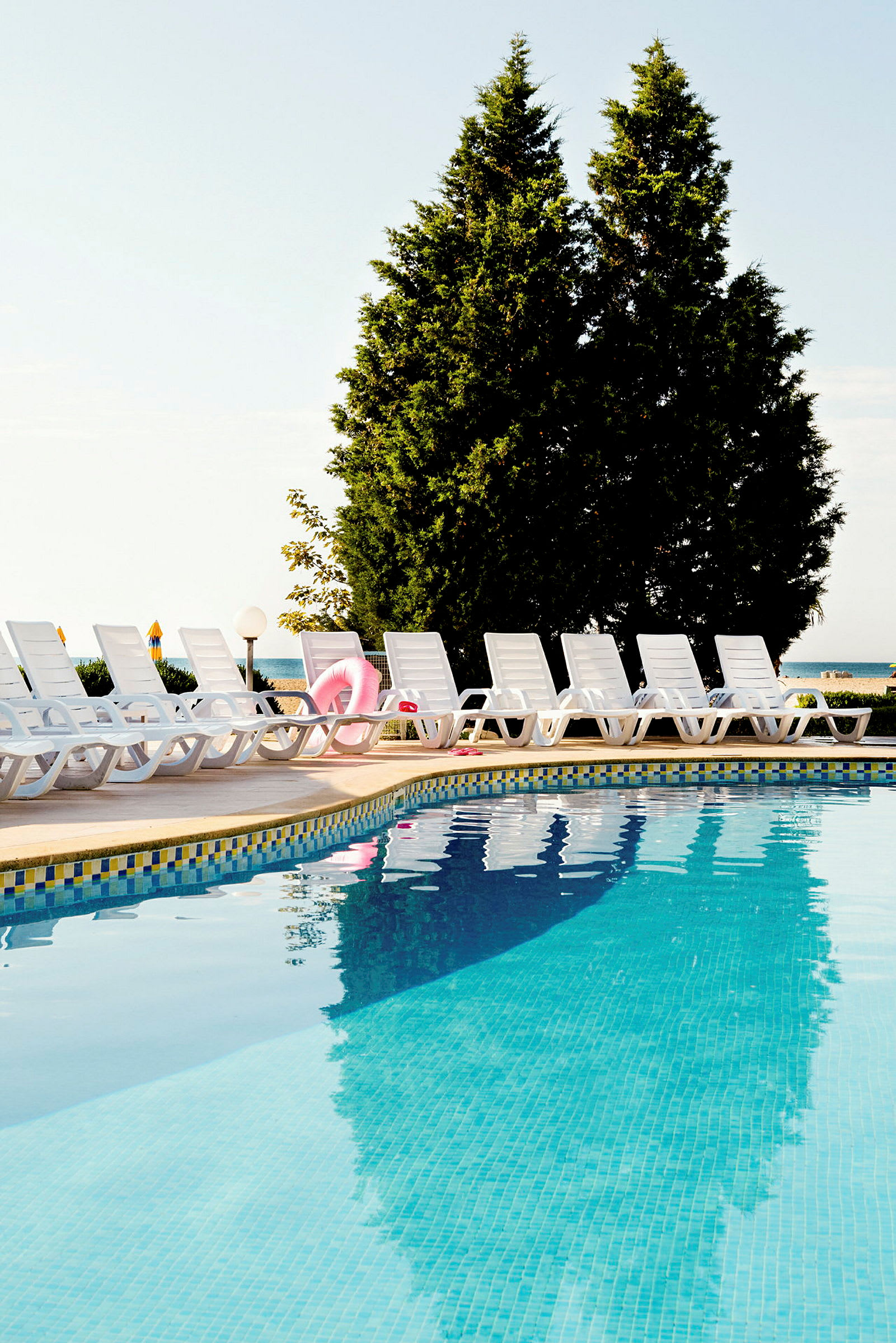 Udendørs pool med liggestole placeret ved kanten under en klar himmel. (AI-genereret tekst)