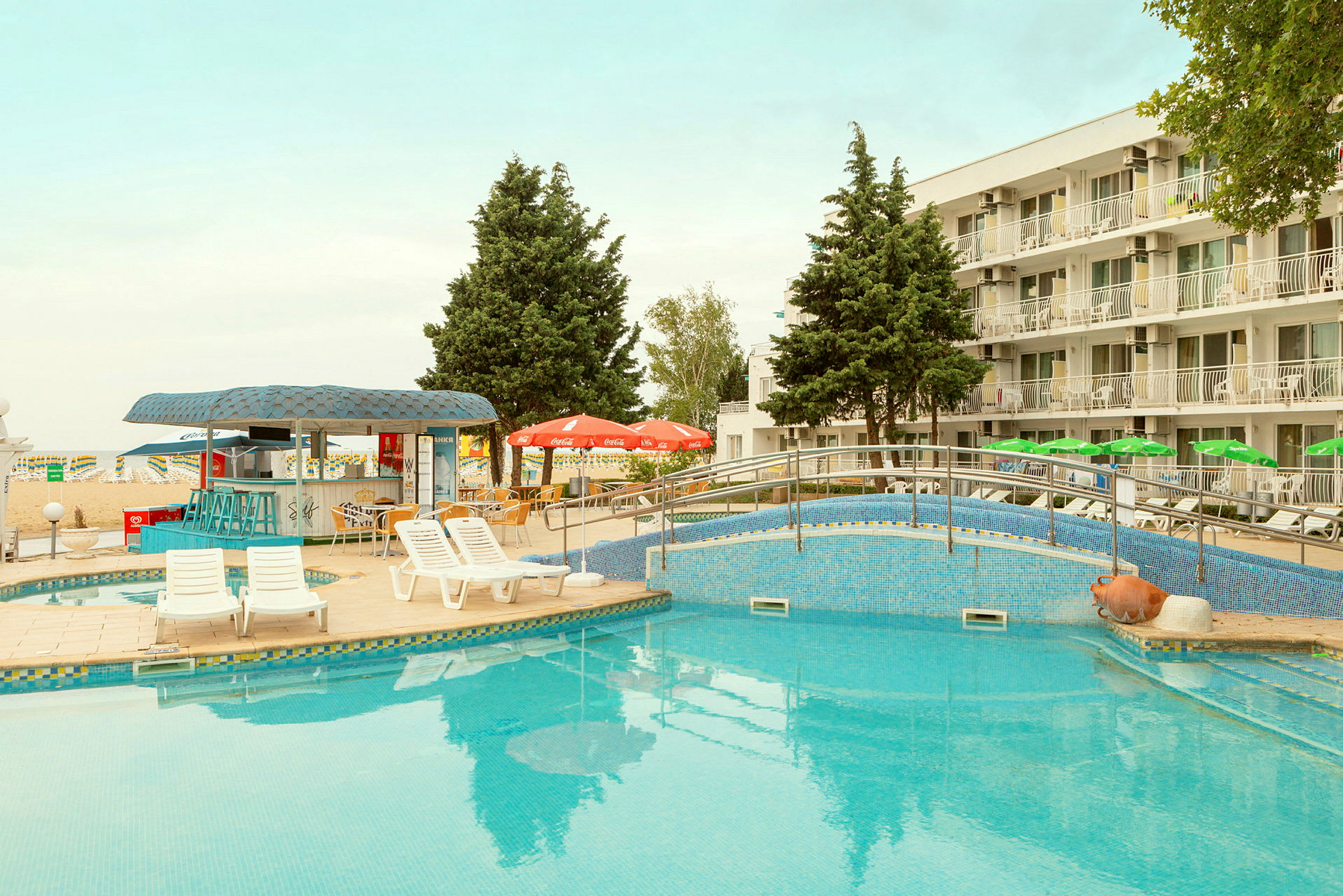 En pool med liggestole og parasoller foran et hotel. (AI-genereret tekst)