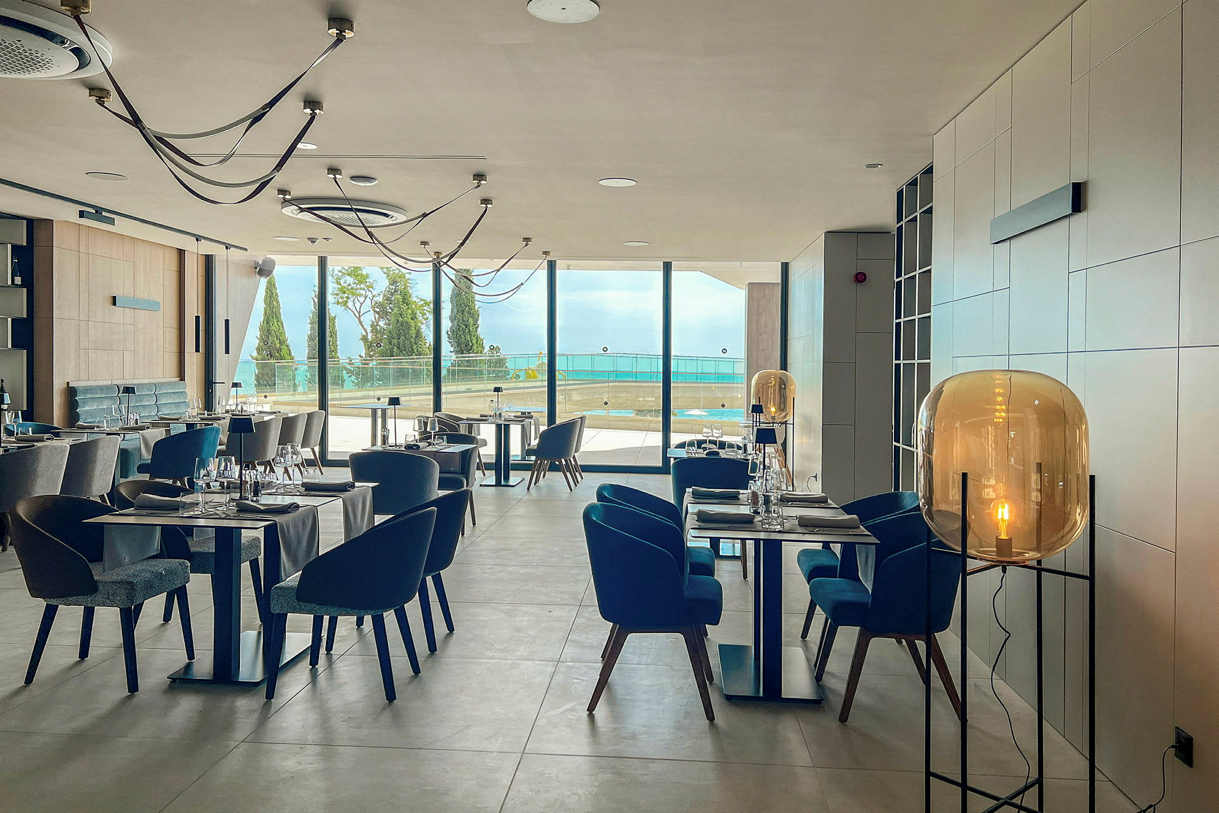 Restaurantinteriør med moderne design, opsatte borde og stole og store vinduer med udsigt over havet. (AI-genereret tekst)