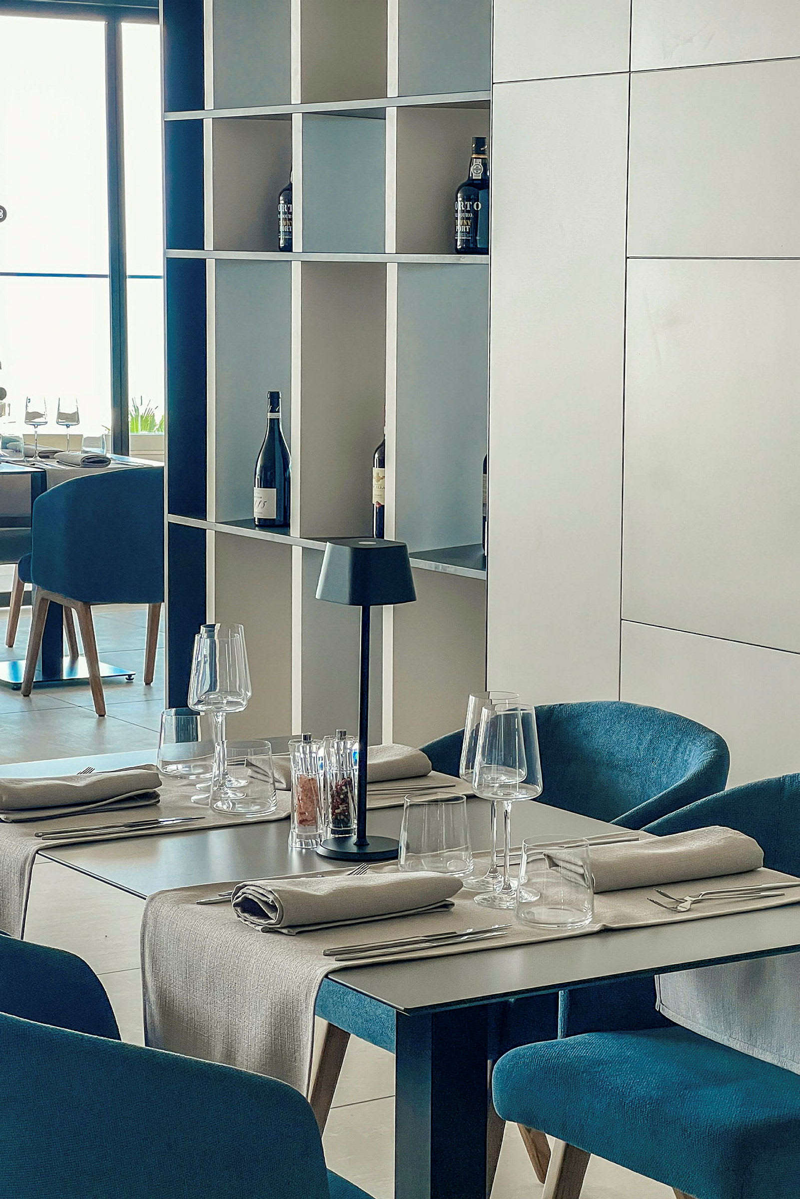 Restaurantbord med borddækning og hylder med vinflasker. (AI-genereret tekst)