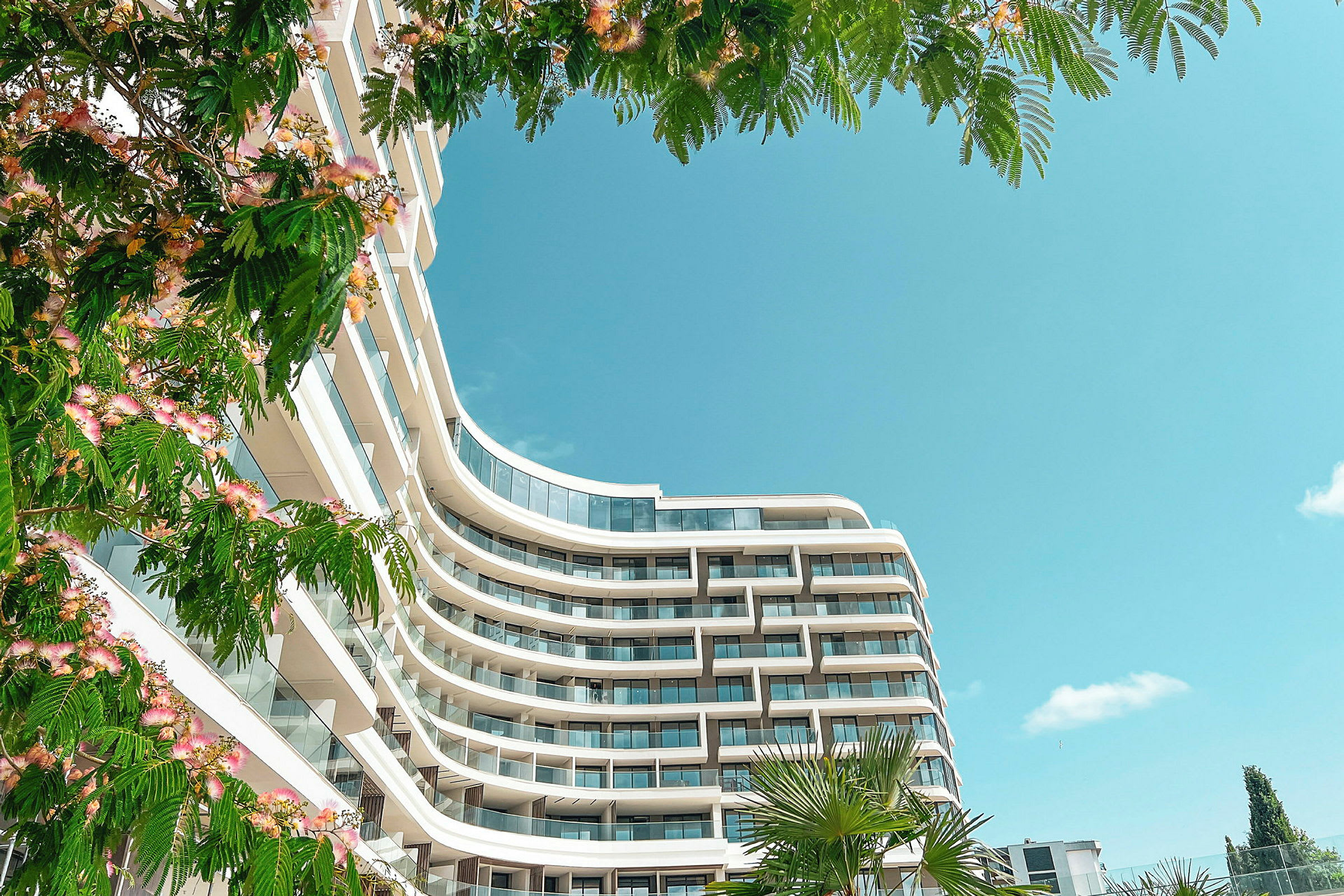 Moderne hotel med altaner, omgivet af grønne omgivelser og blå himmel. (AI-genereret tekst)