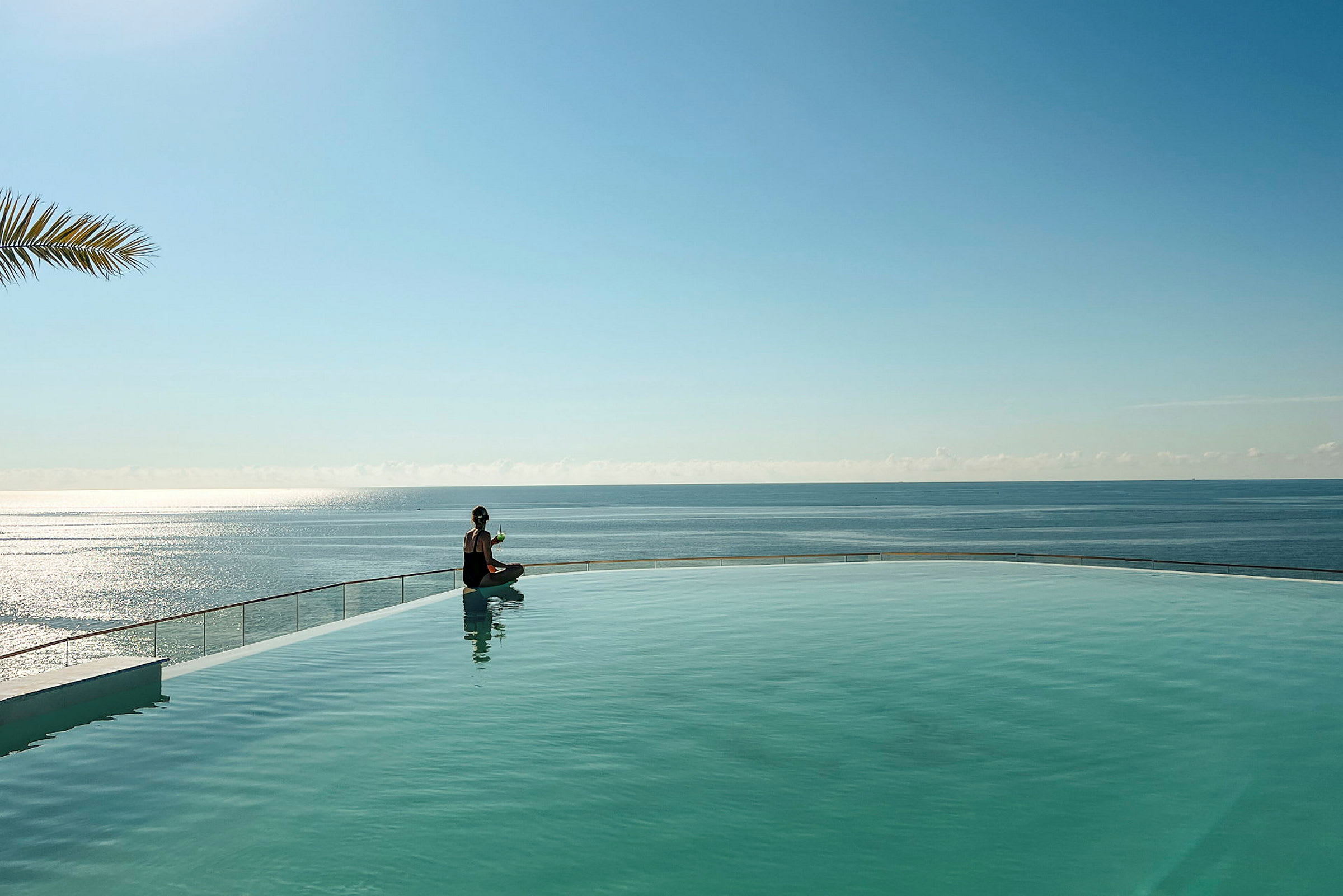 En person sidder ved kanten af en pool med havet i baggrunden. (AI-genereret tekst)