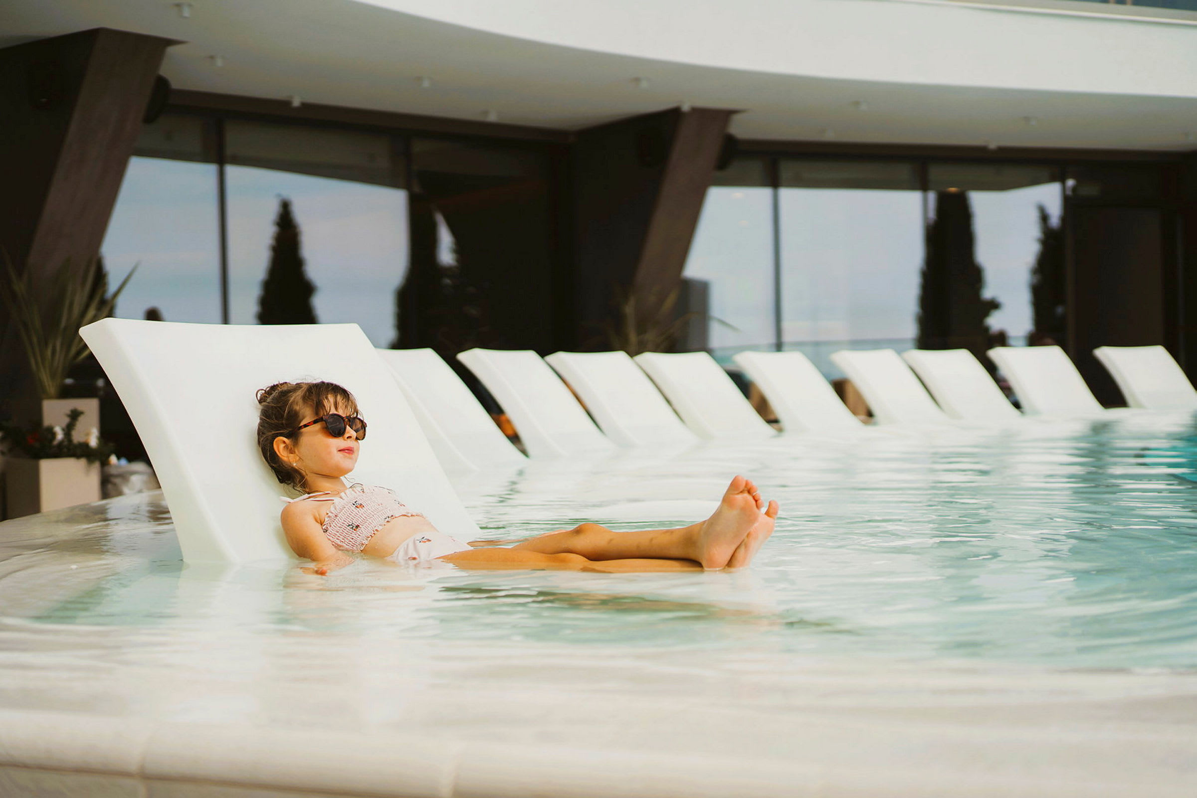 Et barn ligger på en liggestol i en pool ved et moderne hotel. (AI-genereret tekst)