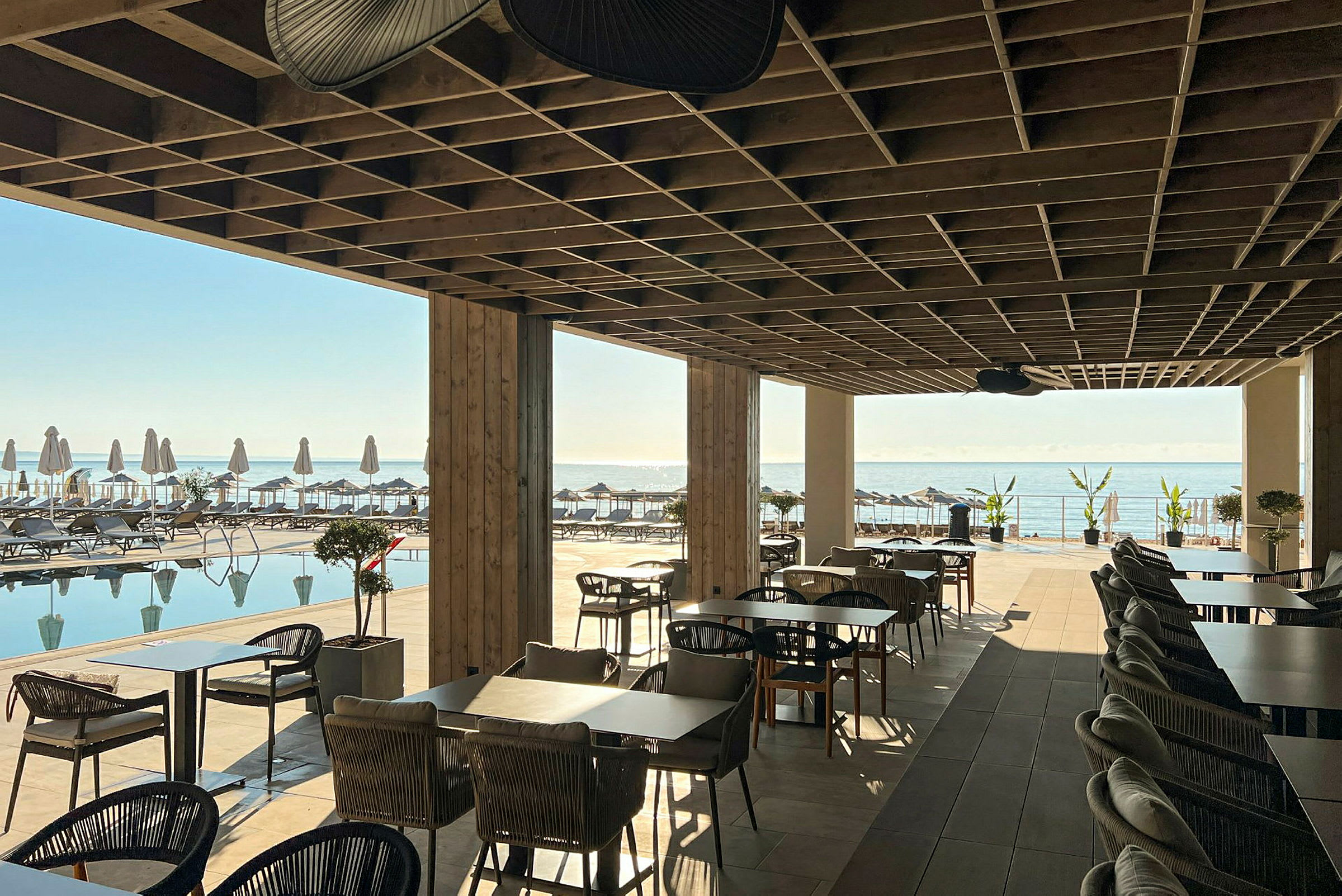 Restaurantområde under tag med udsigt over pool og hav. (AI-genereret tekst)