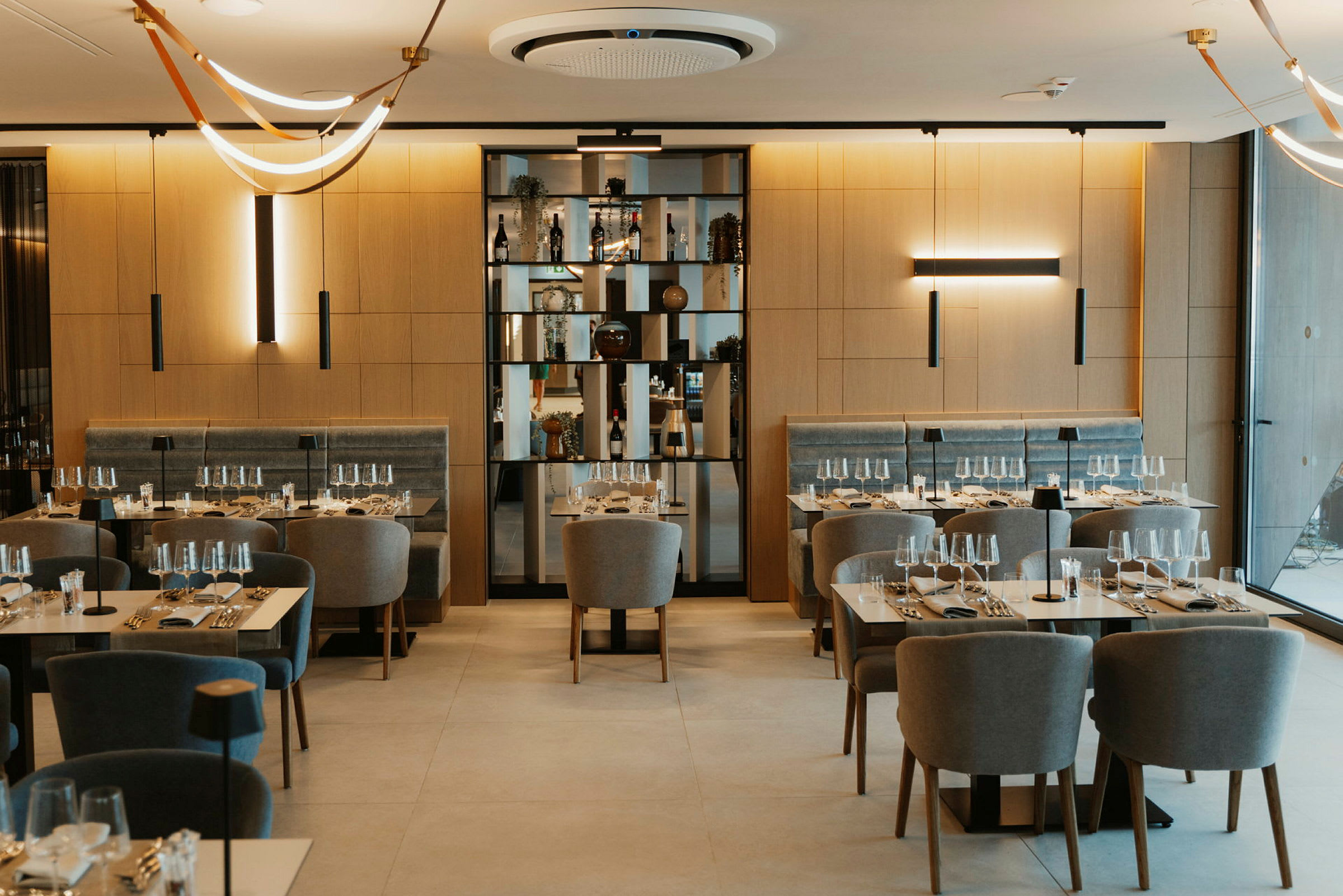 Restaurant med dækkede borde og komfortable stole samt dekorative lamper i loftet. (AI-genereret tekst)