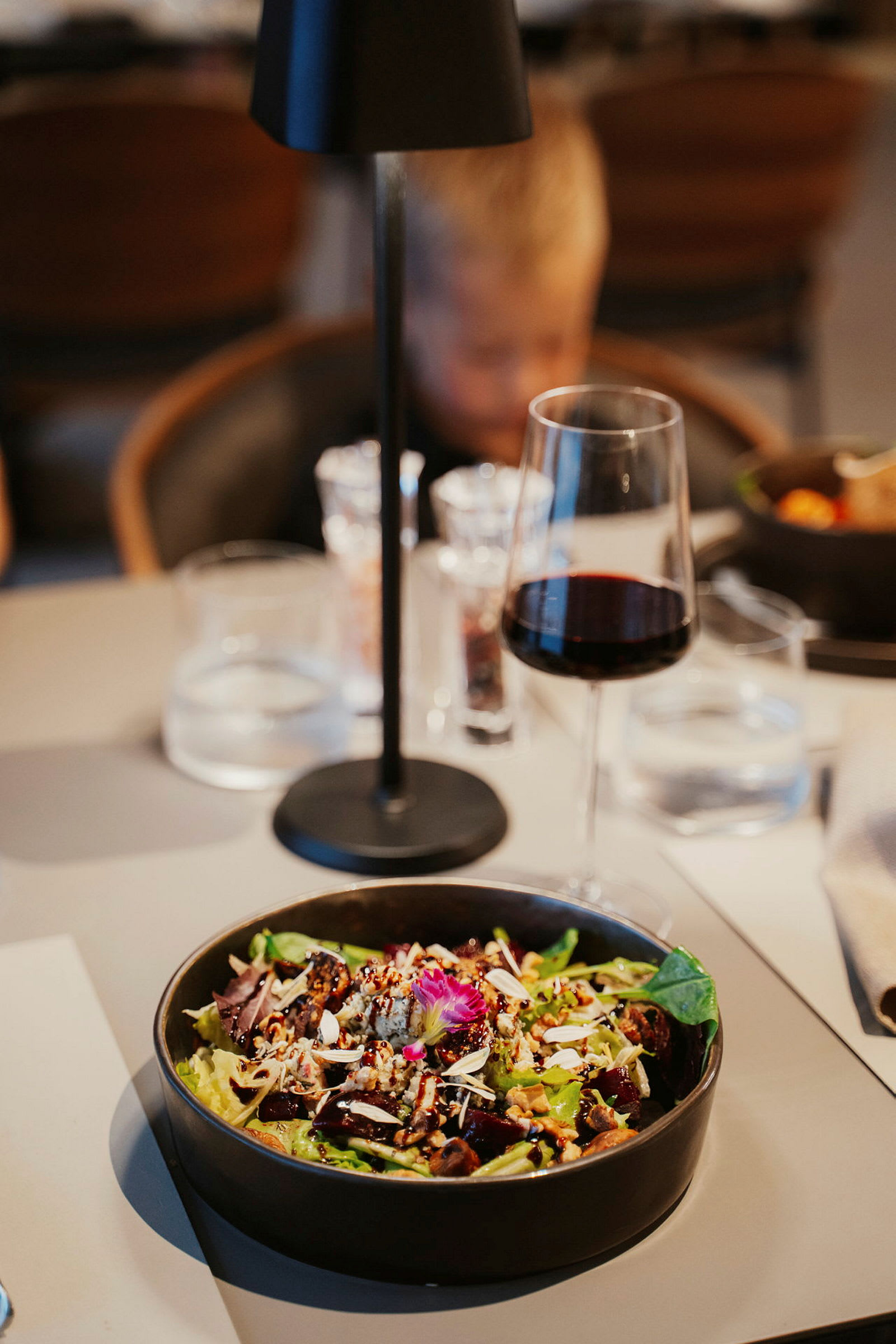 En skål med salat pyntet med nødder og blomster på et opdækket bord. (AI-genereret tekst)