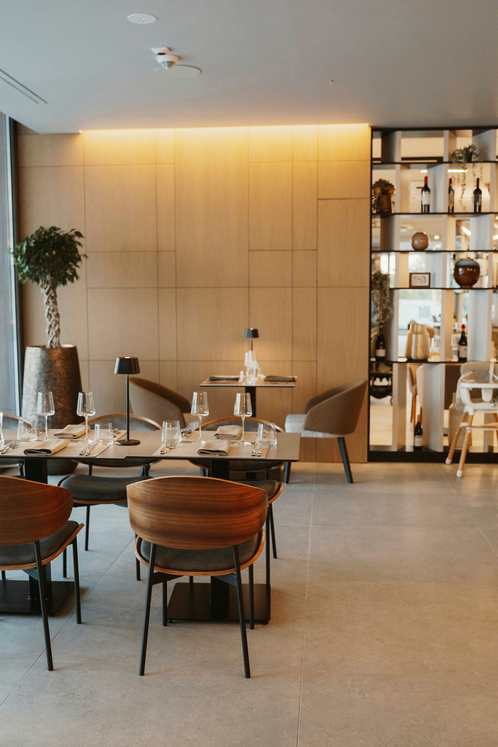 En moderne restaurant med træpaneler, elegante borde og stole samt glas og tallerkener klar til servering. (AI-genereret tekst)