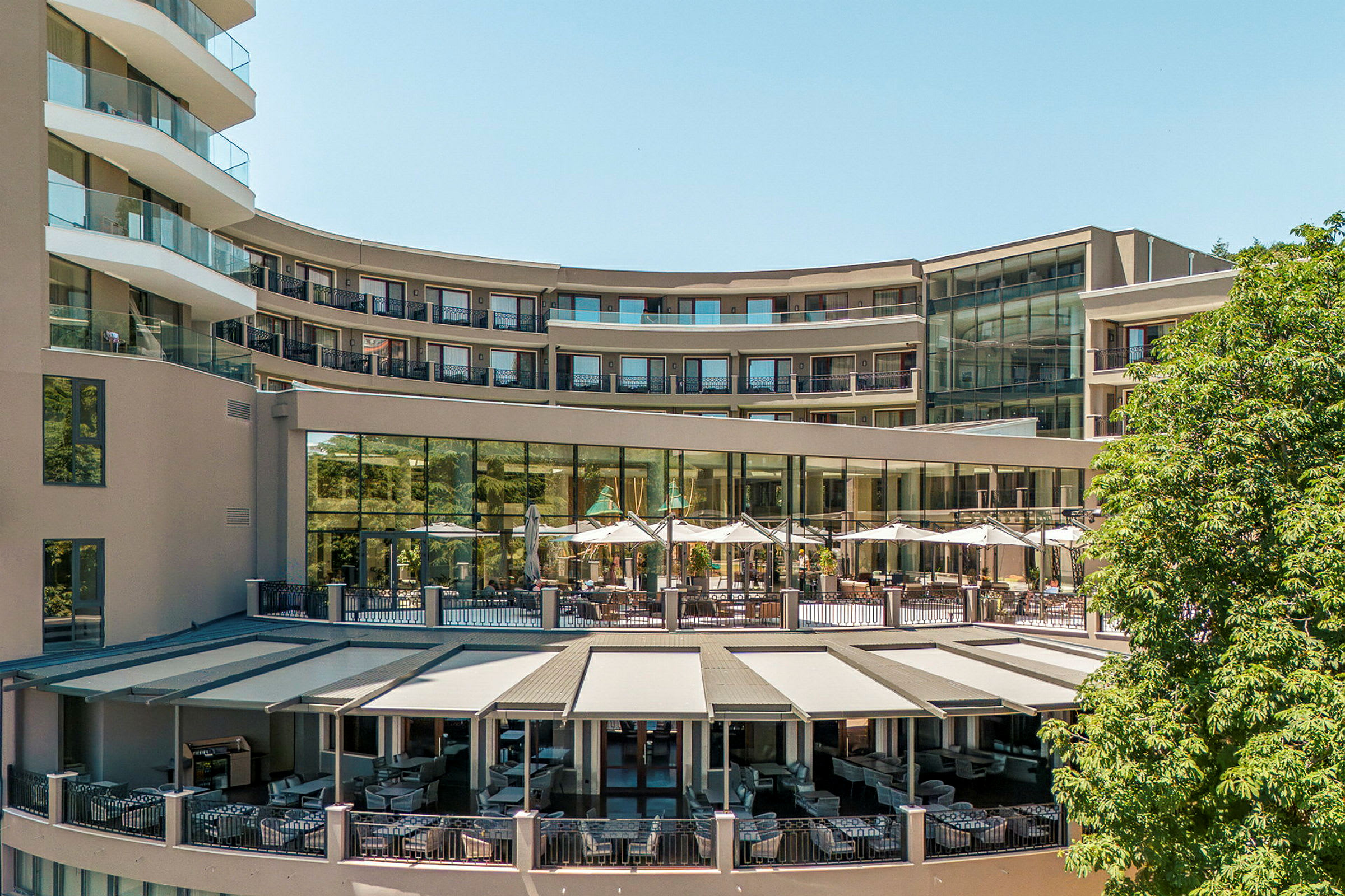 Hotelbygning med udendørs terrasse og solafskærmning. (AI-genereret tekst)