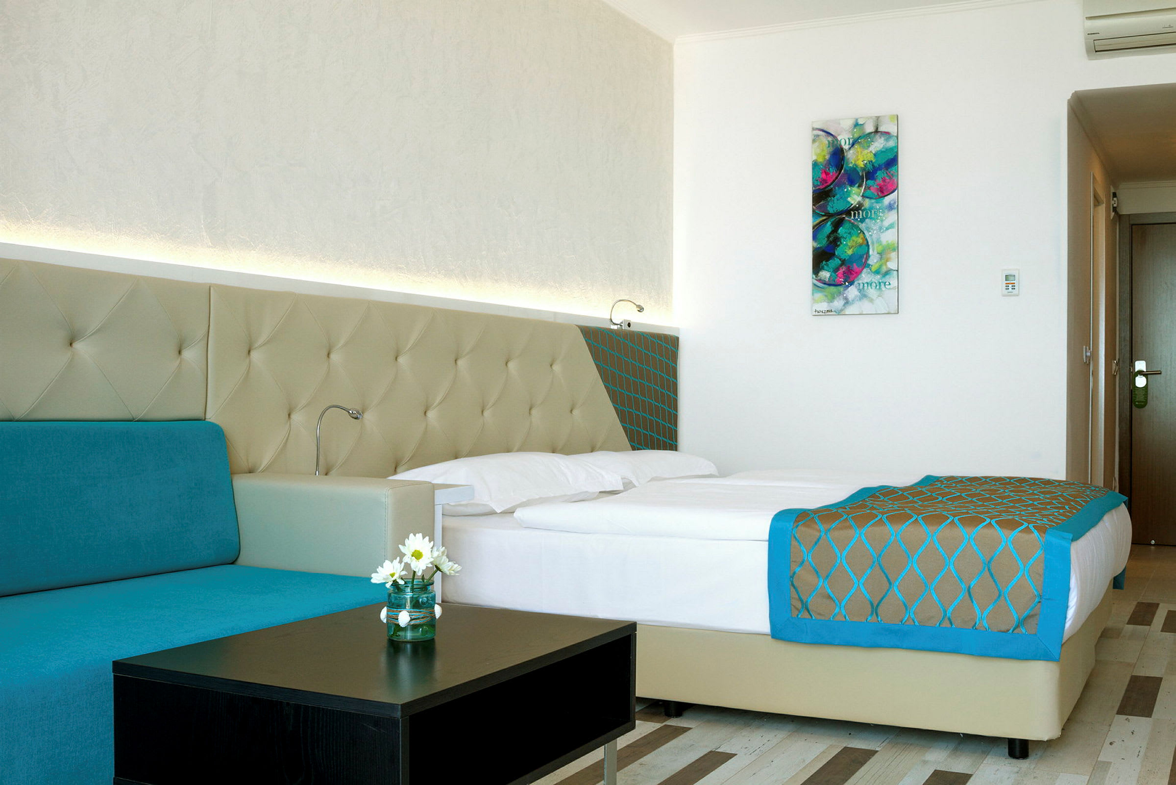 Et moderne hotelværelse med en dobbeltseng, turkis sofa og vægkunst. (AI-genereret tekst)